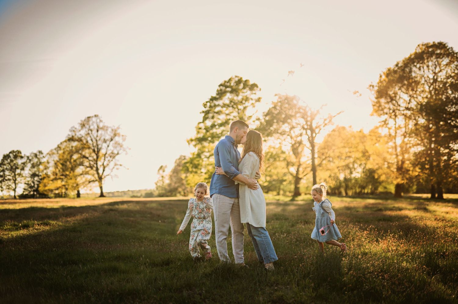 A family walks together in a sun-drenched field during golden hour.