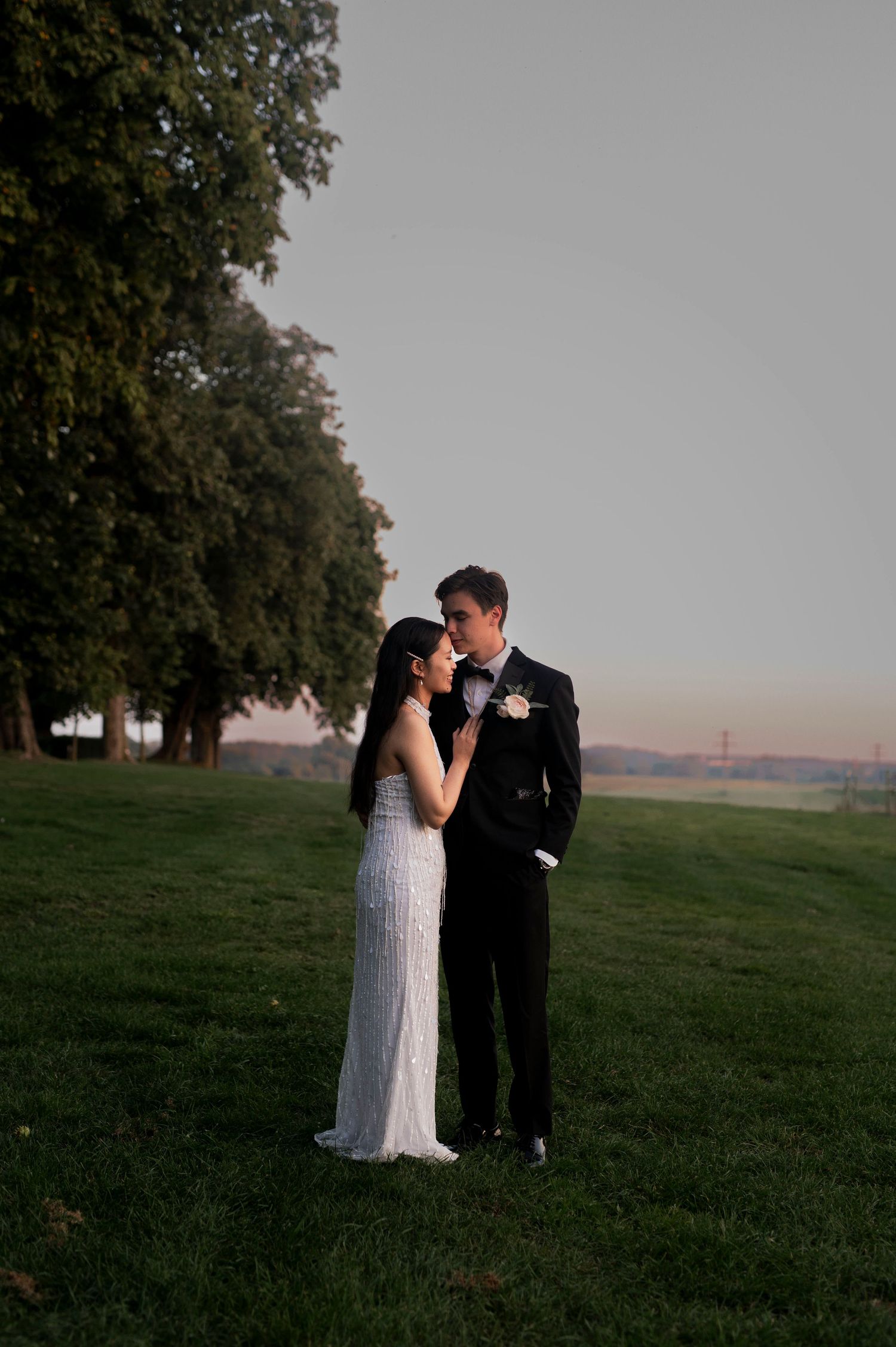 Newlyweds share intimate moment on grassy hill at sunset.