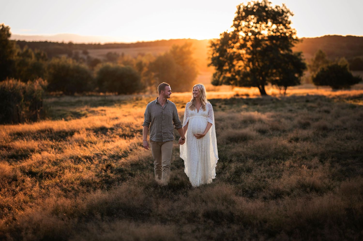 Two figures walk hand in hand through a golden field at sunset with a lone tree silhouetted in the background.