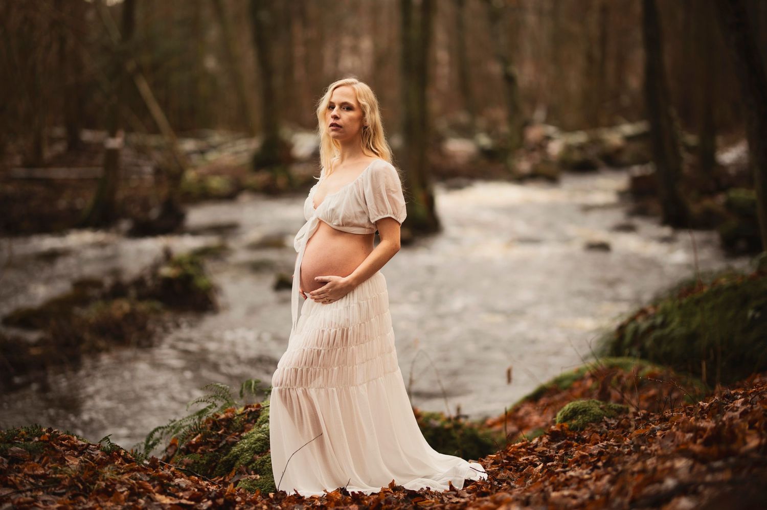Vacker gravid kvinna på fotografering vid en bäck. Fotograf är Lovestories By Sara.