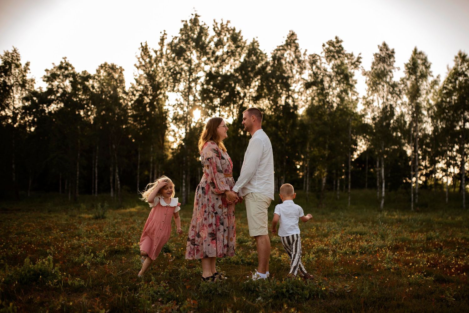 Family standing together in field at sunset with tree silhouettes in background.