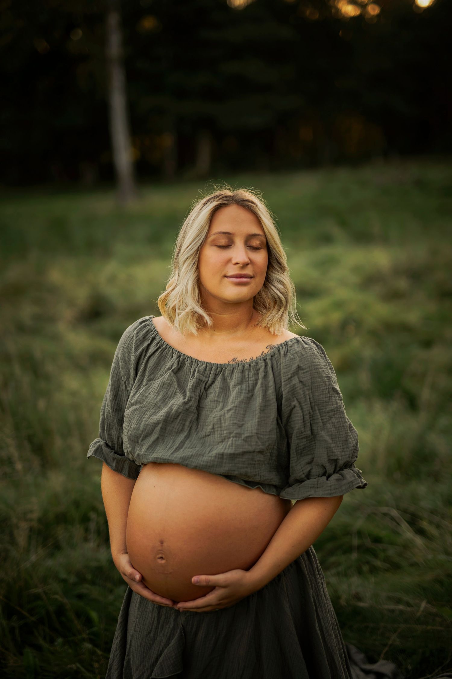 Intimate maternity portrait showing pregnant belly against gray dress in outdoor natural setting.