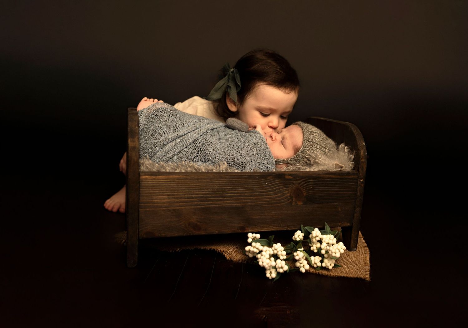 Studio portrait of baby in wooden box with white flowers.