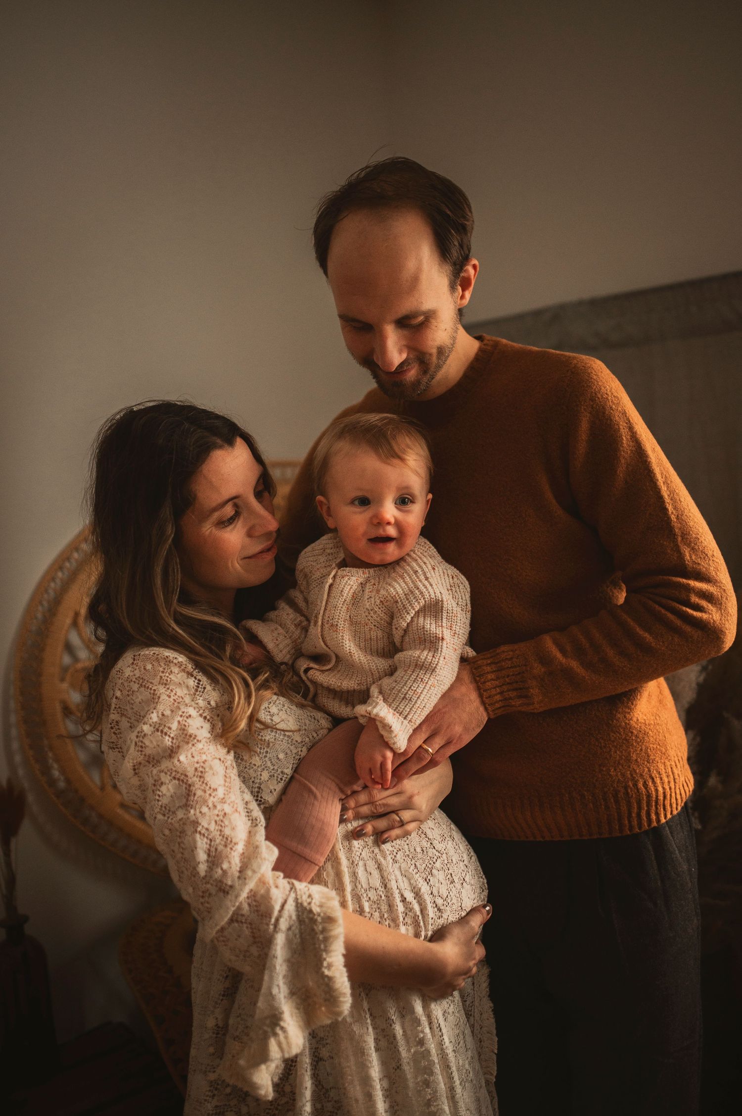 Cozy family portrait with baby in matching neutral tones and warm lighting.