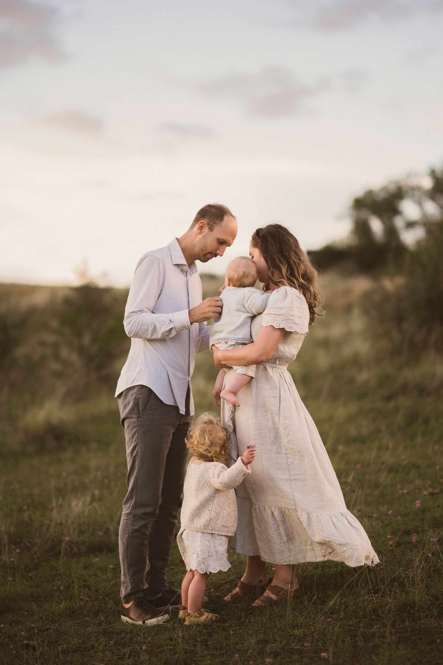 Family shares intimate moment together on hillside during golden hour.