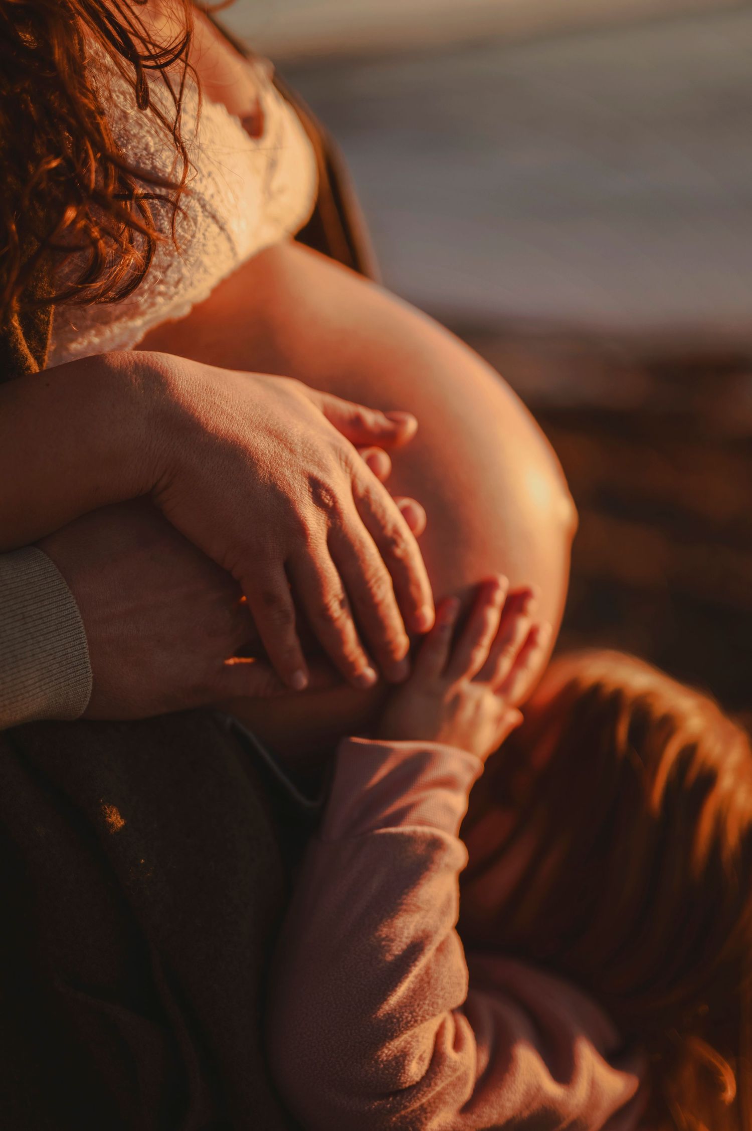 Close-up of hands tenderly touching a pregnant belly in warm sunset light.