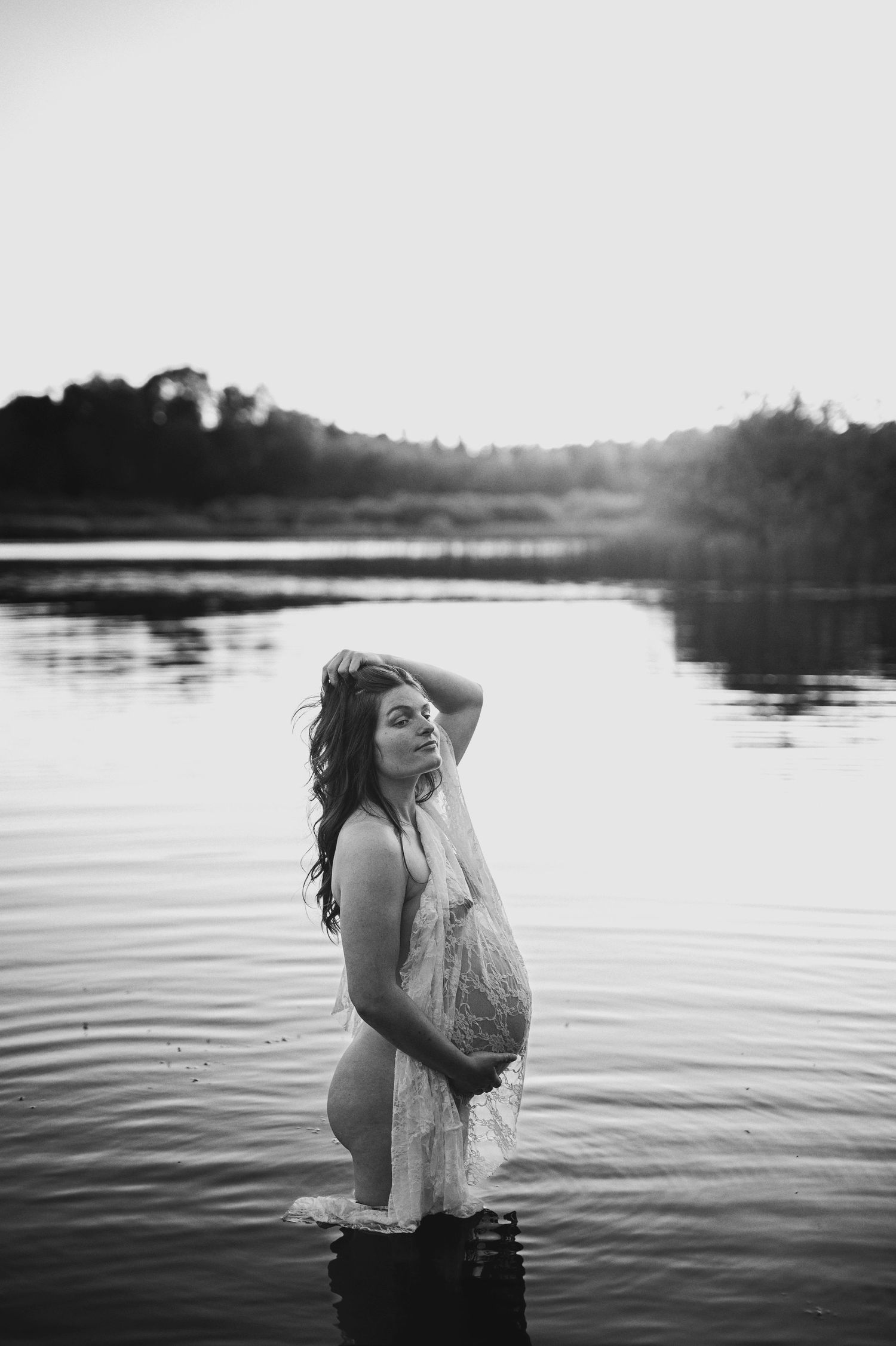 Artistic maternity photo shoot in calm waters with dramatic black and white tones.