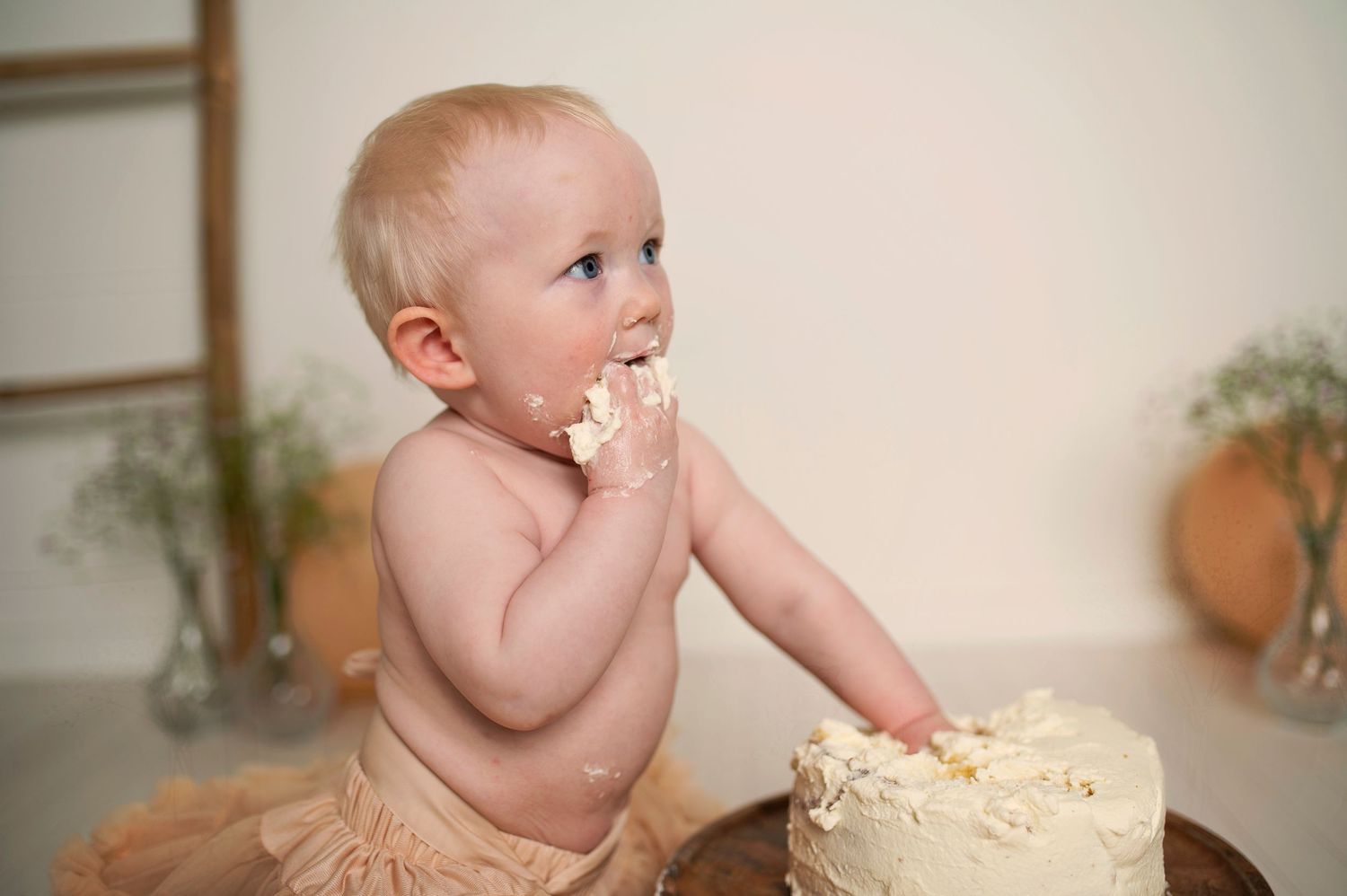 Baby enthusiastically tasting white frosting from birthday cake during cake smash session.
