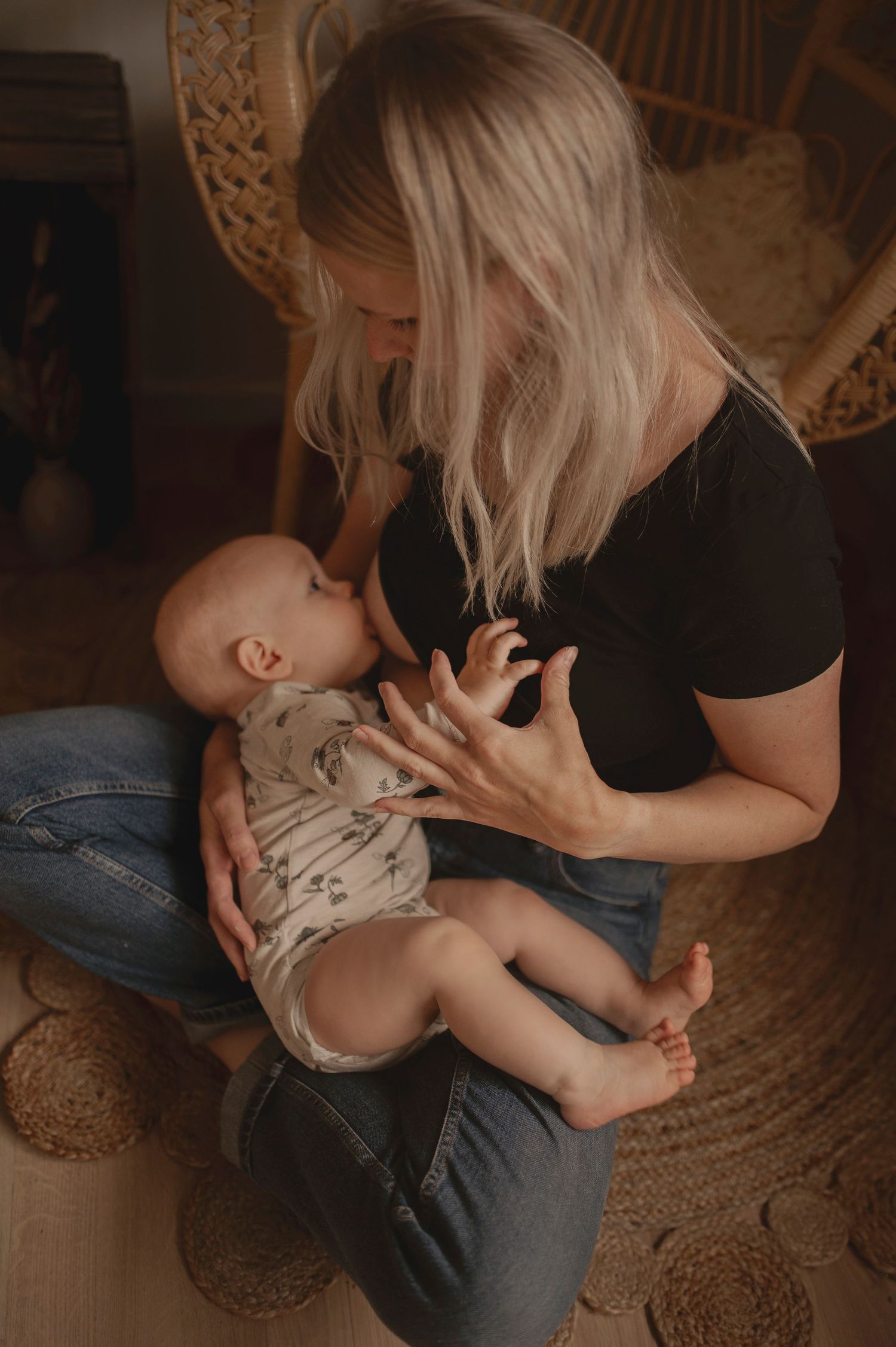 Gentle nurturing moment between parent and baby in front of a woven chair.