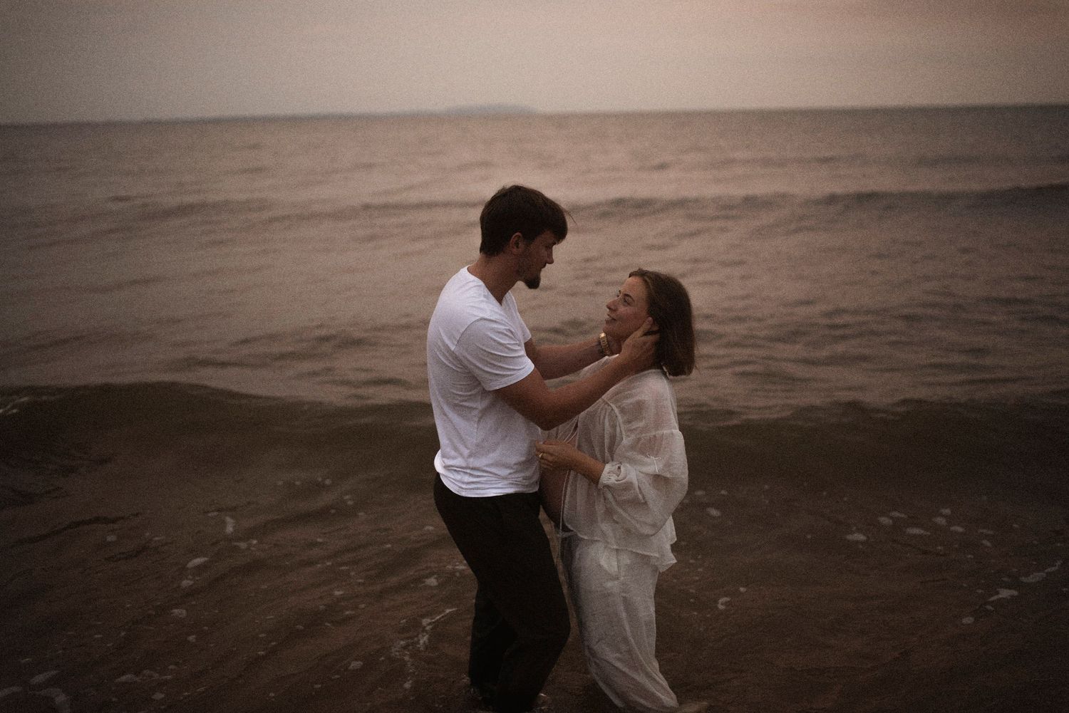 A tender embrace between two people on a moody beach at dusk.