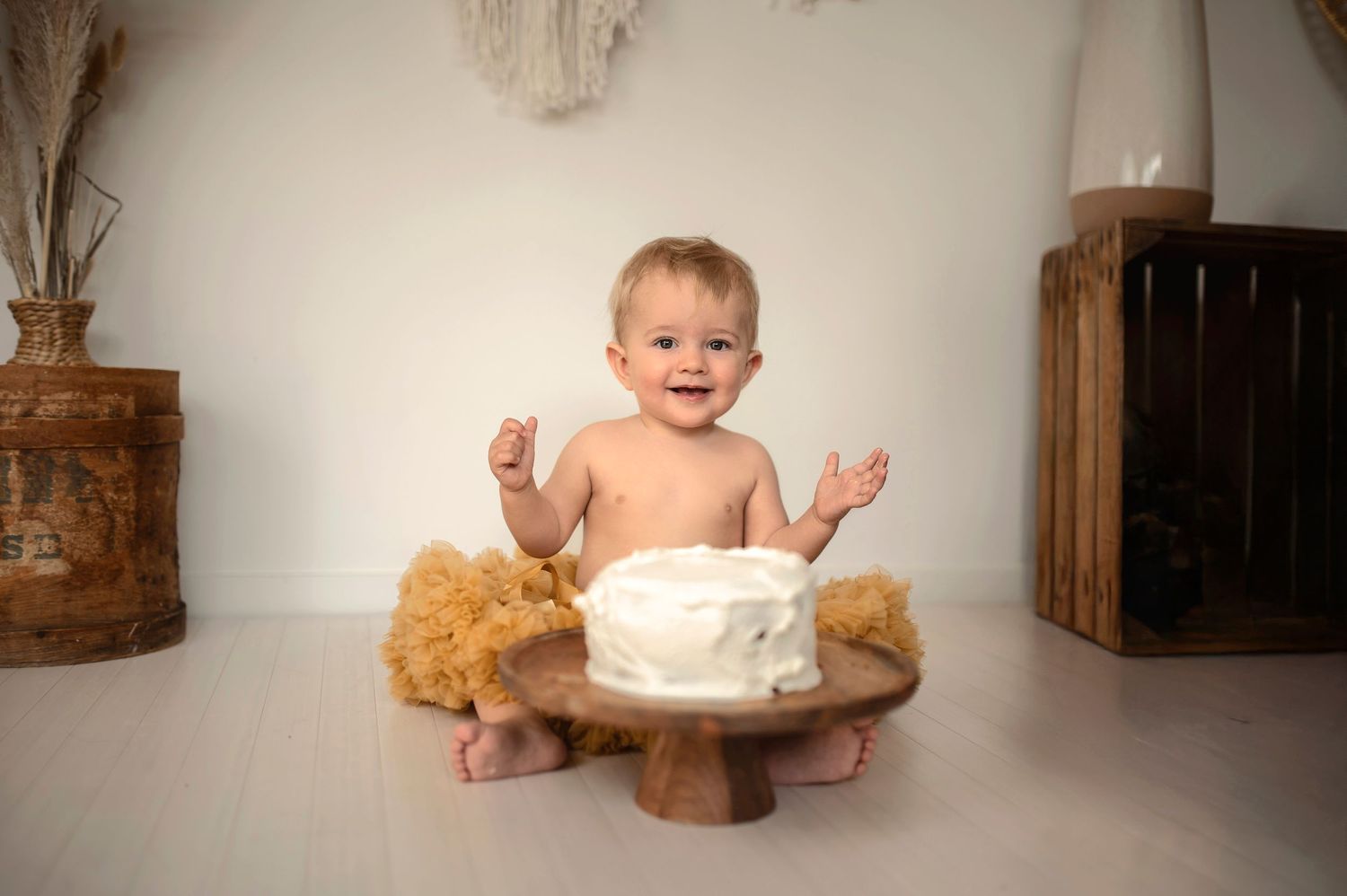 A baby sits on the floor with a smash cake and teddy bear during a first birthday photo session.