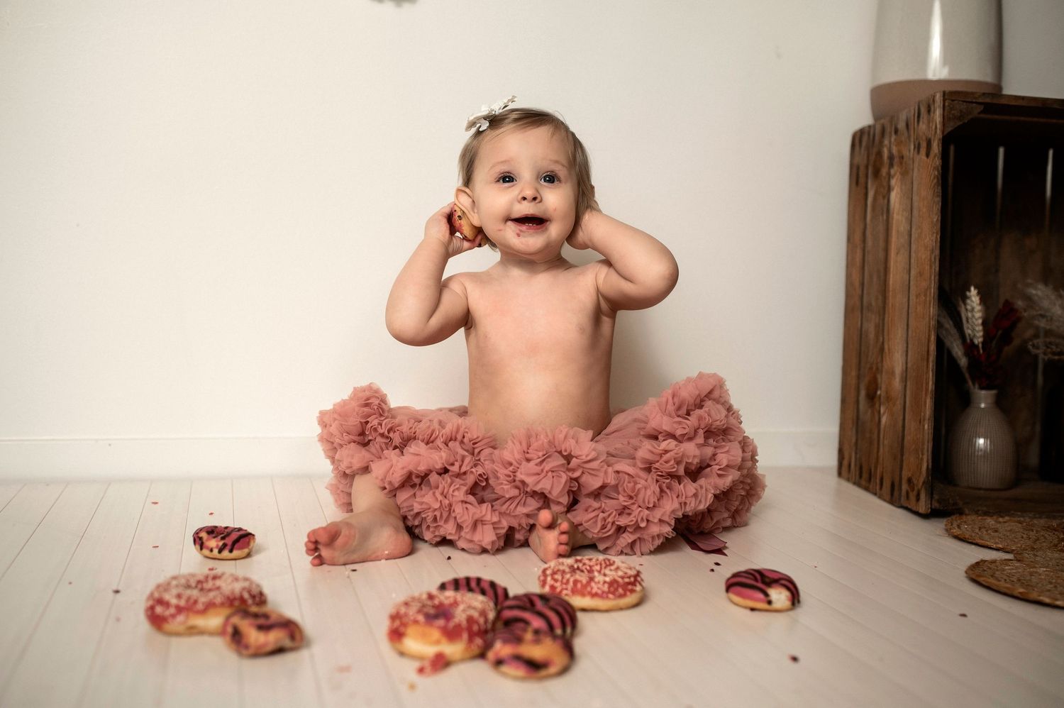 A series of photos showing a baby's first birthday cake smash session with a pink frosted cake and matching tutu.