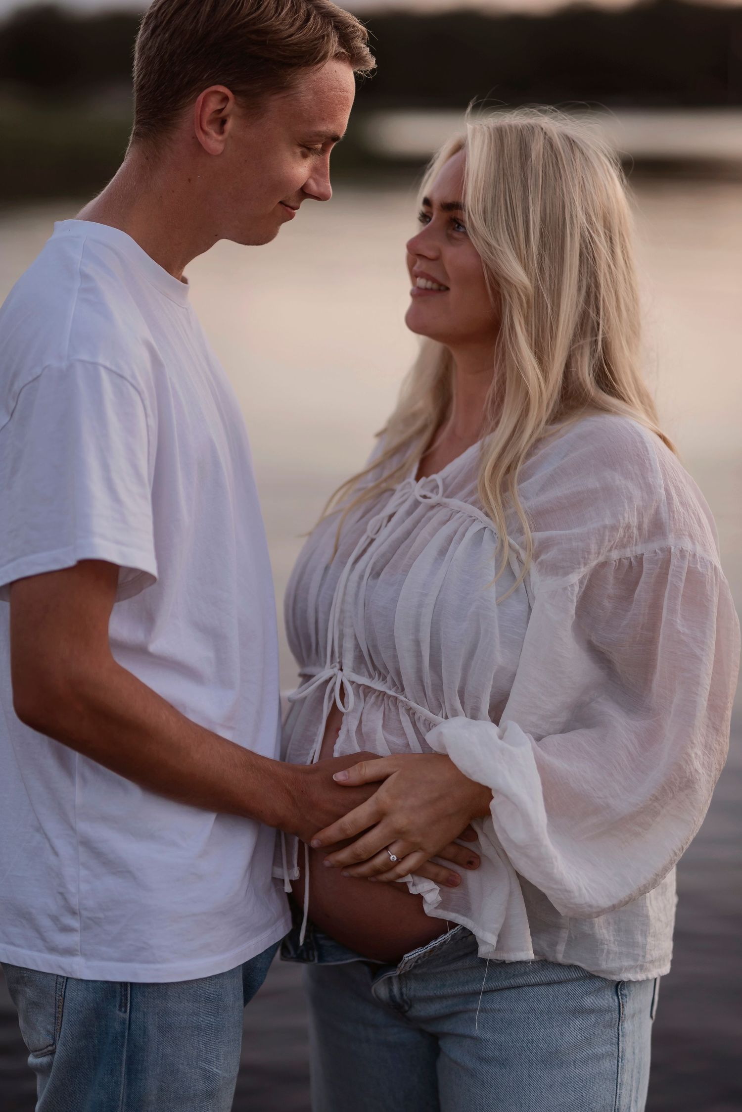 An intimate moment between a couple on the beach during golden hour wearing white and denim.