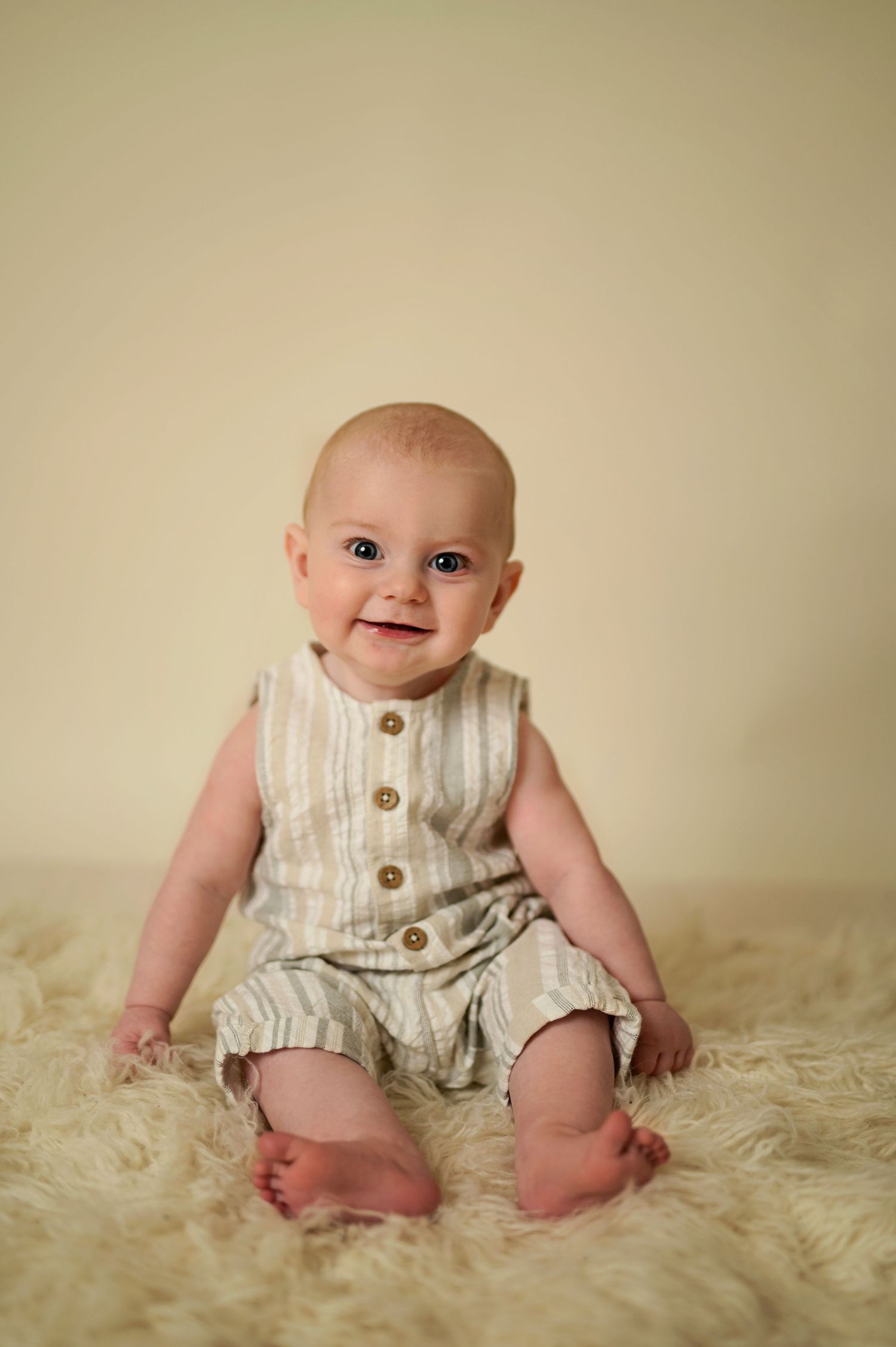 Baby wearing striped romper sitting on furry rug.