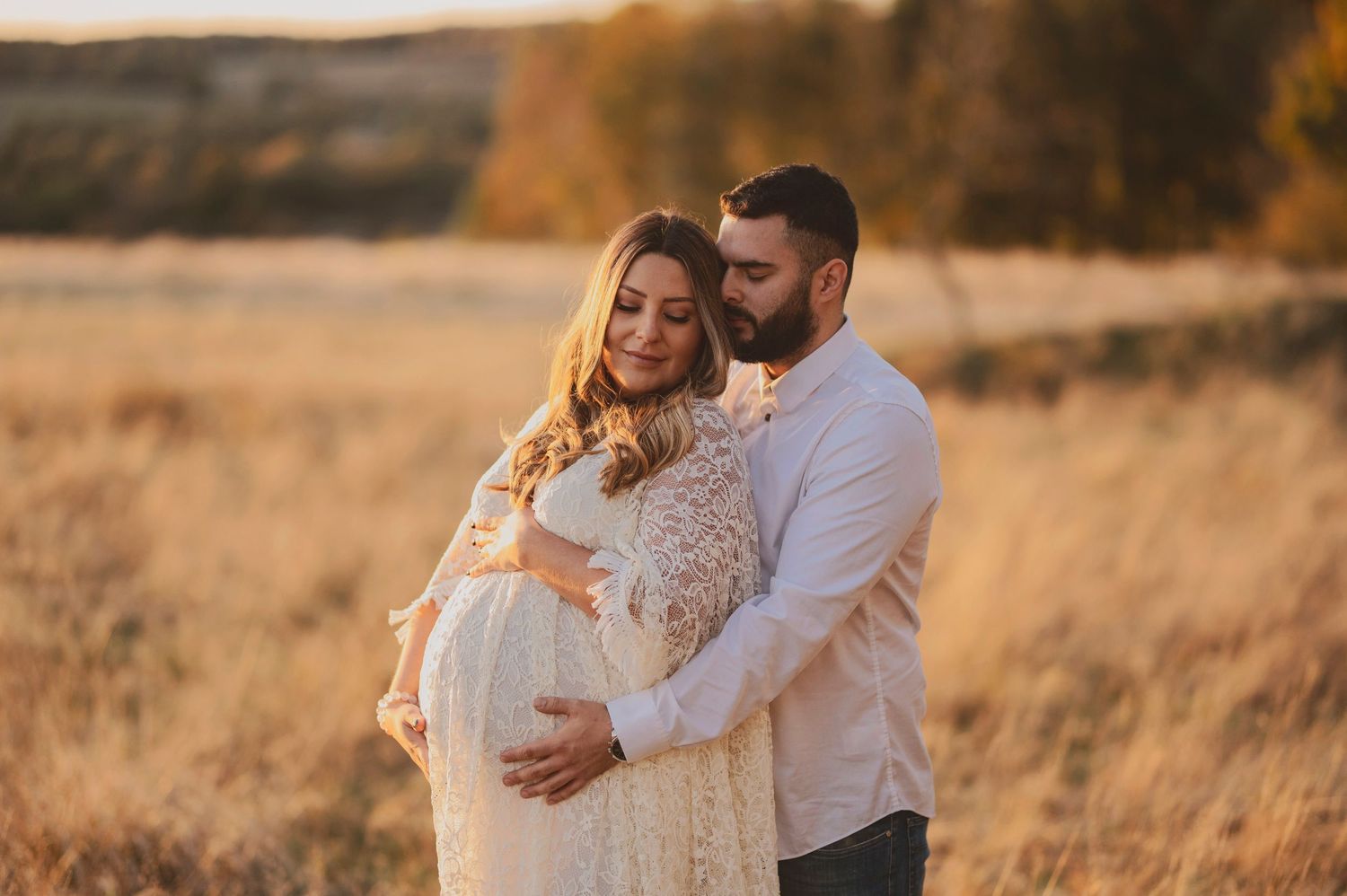 Couple in white clothing embracing in golden sunlit field.
