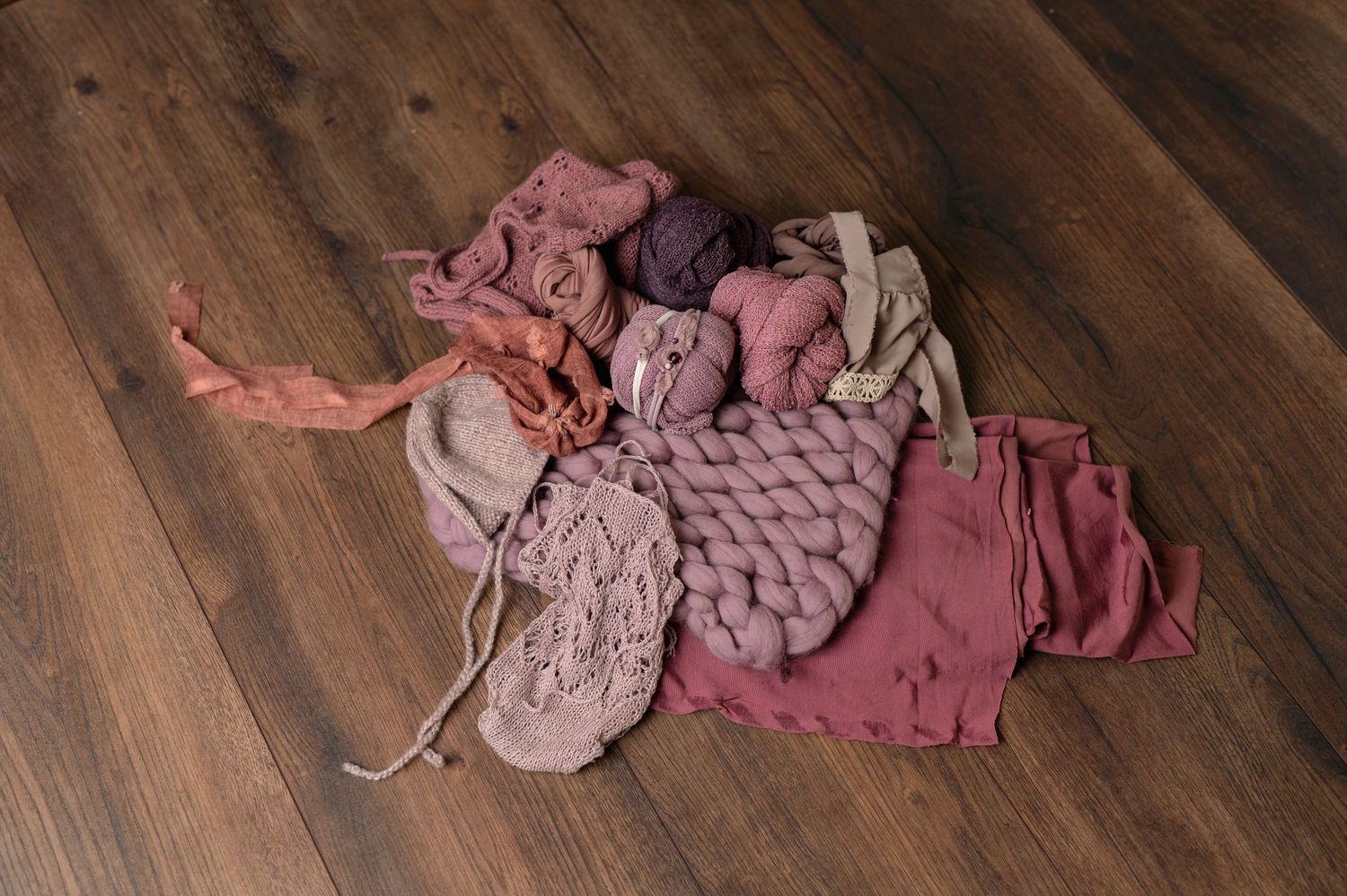Pink and mauve baby clothes and accessories arranged on wooden floor.
