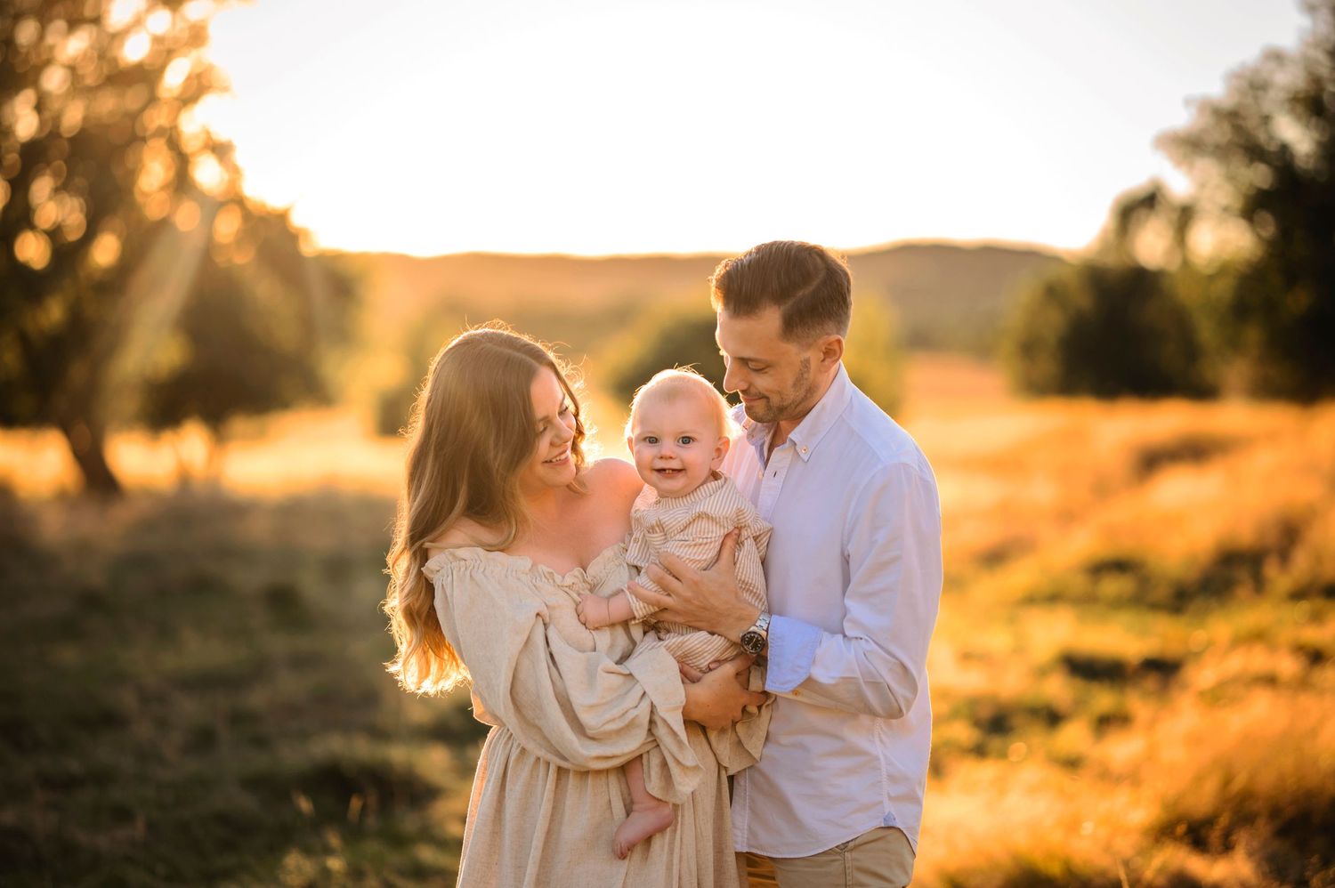 A happy family embraces in a golden sunlit field during sunset.