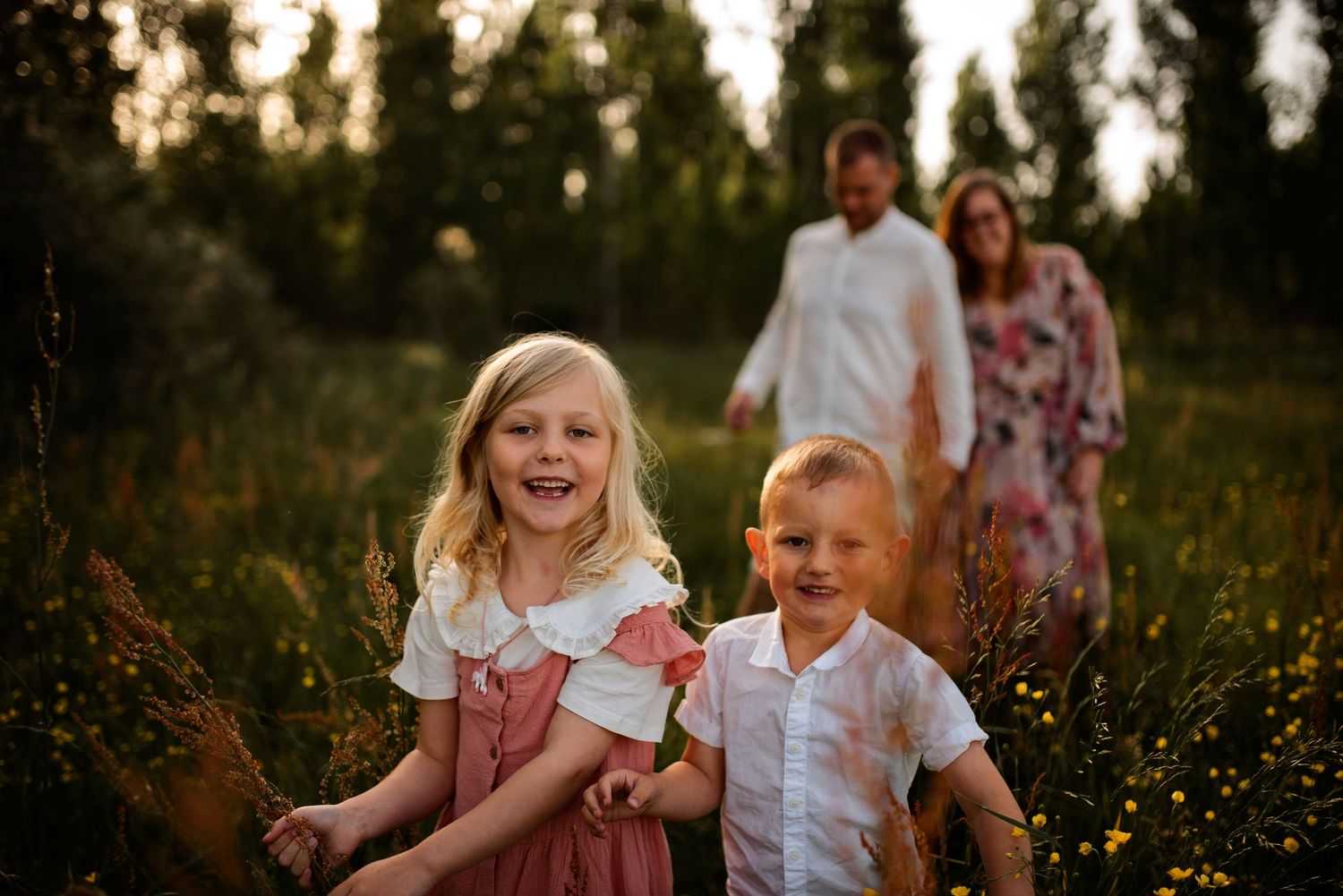 Playful moment in meadow with children in foreground and parents in background.