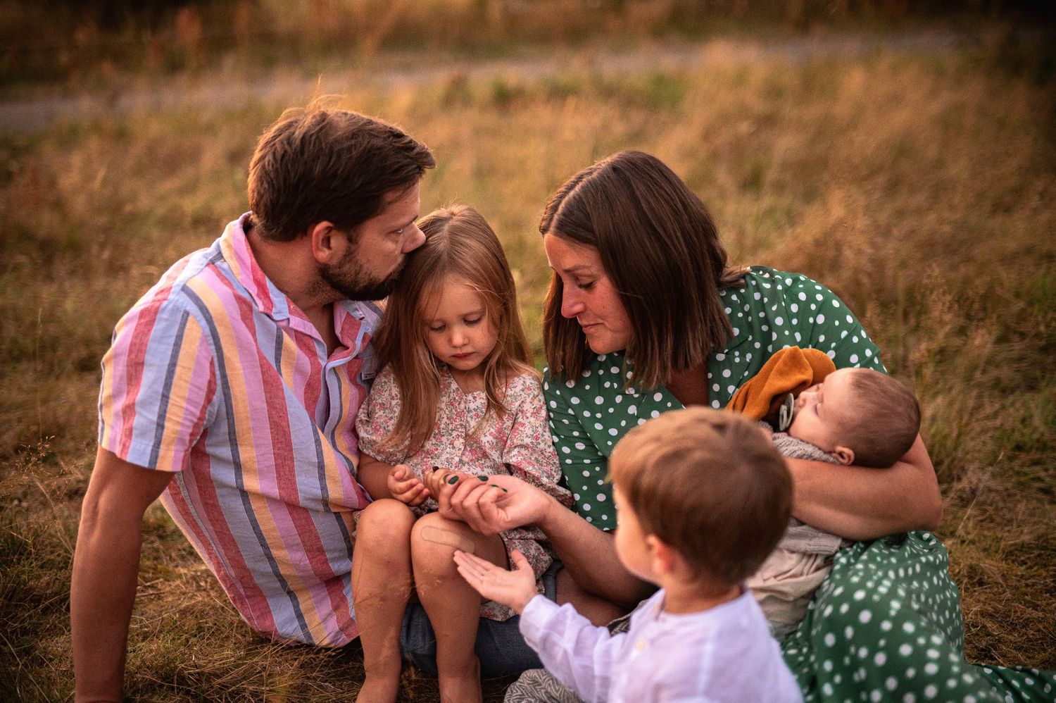 Family sharing an intimate moment together on a blanket in a summer field.