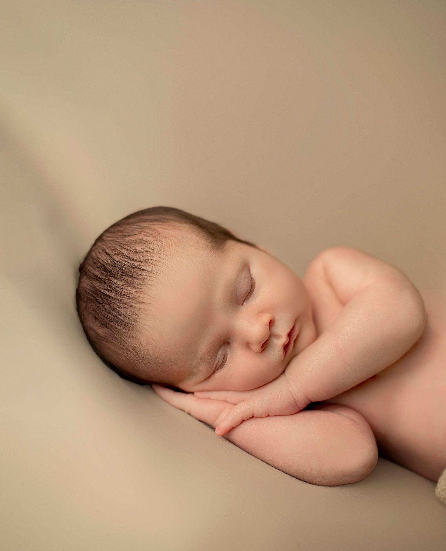 Peaceful newborn baby sleeping on beige background in studio setting with gentle lighting.