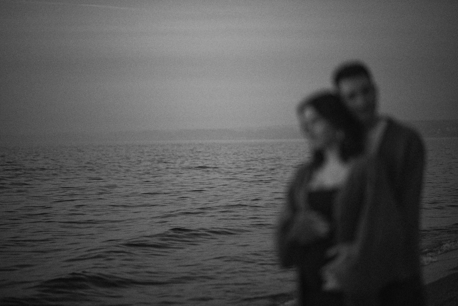 A romantic silhouette of a couple stands together against a misty ocean horizon in black and white.