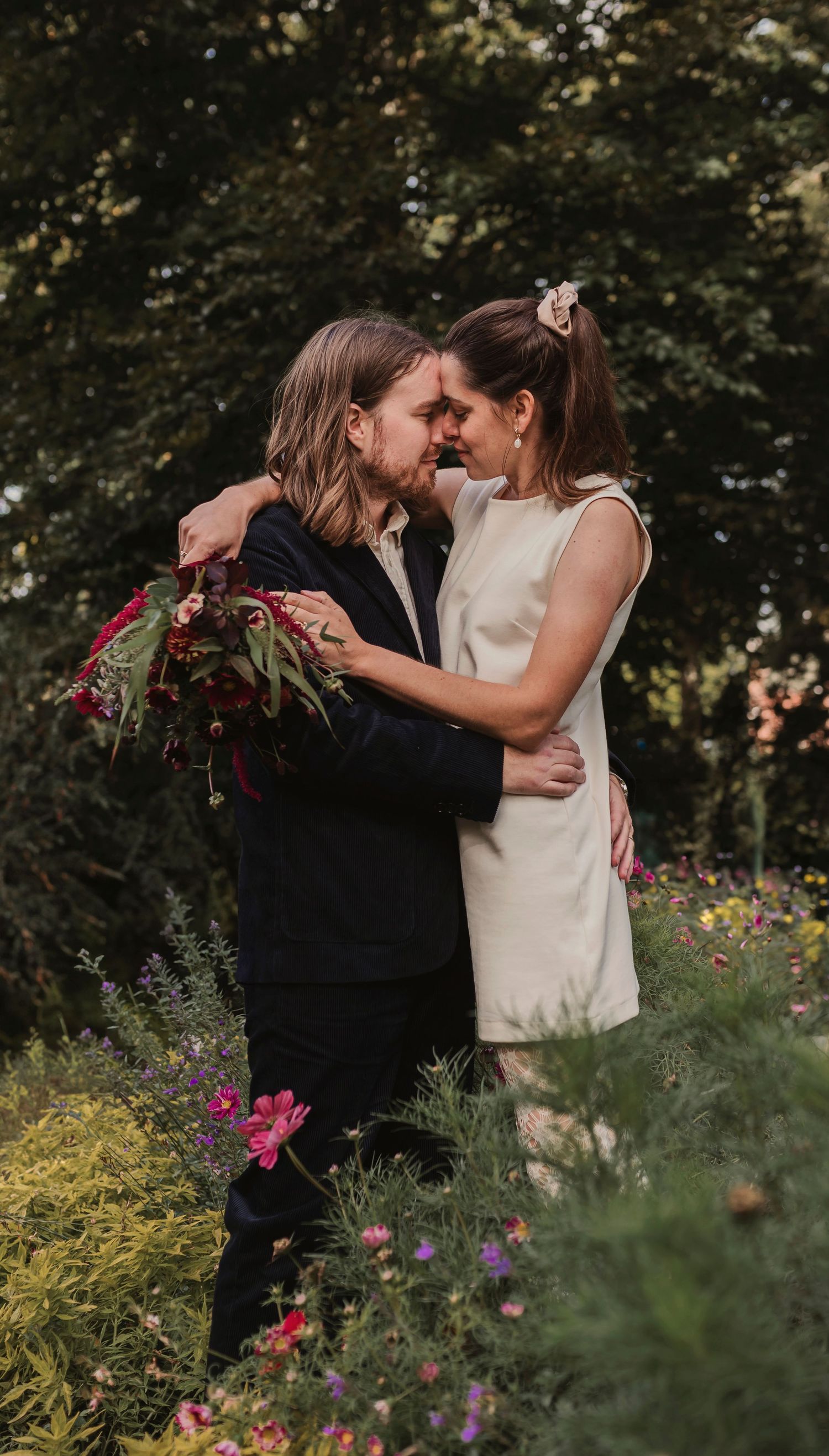 Couple embracing in garden surrounded by colorful flowers and greenery.