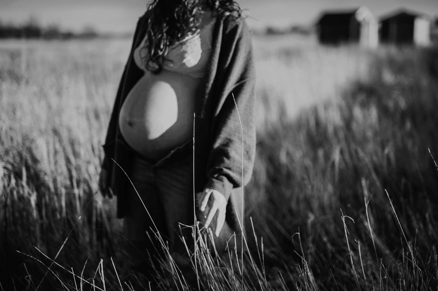 Black and white portrait of pregnant figure standing in natural field setting.