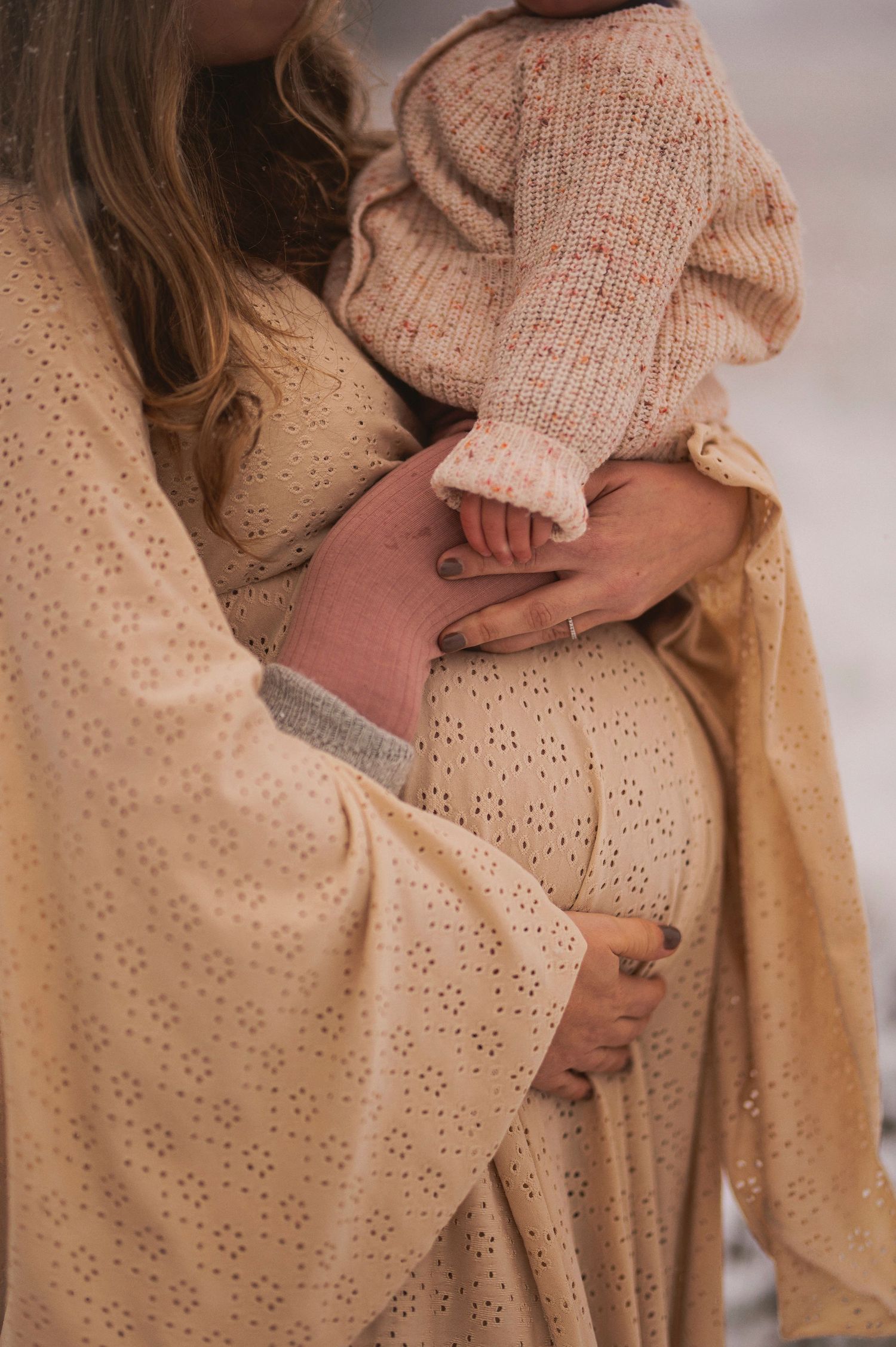 Close-up detail of hands holding in cream-colored knitwear against textured fabric.