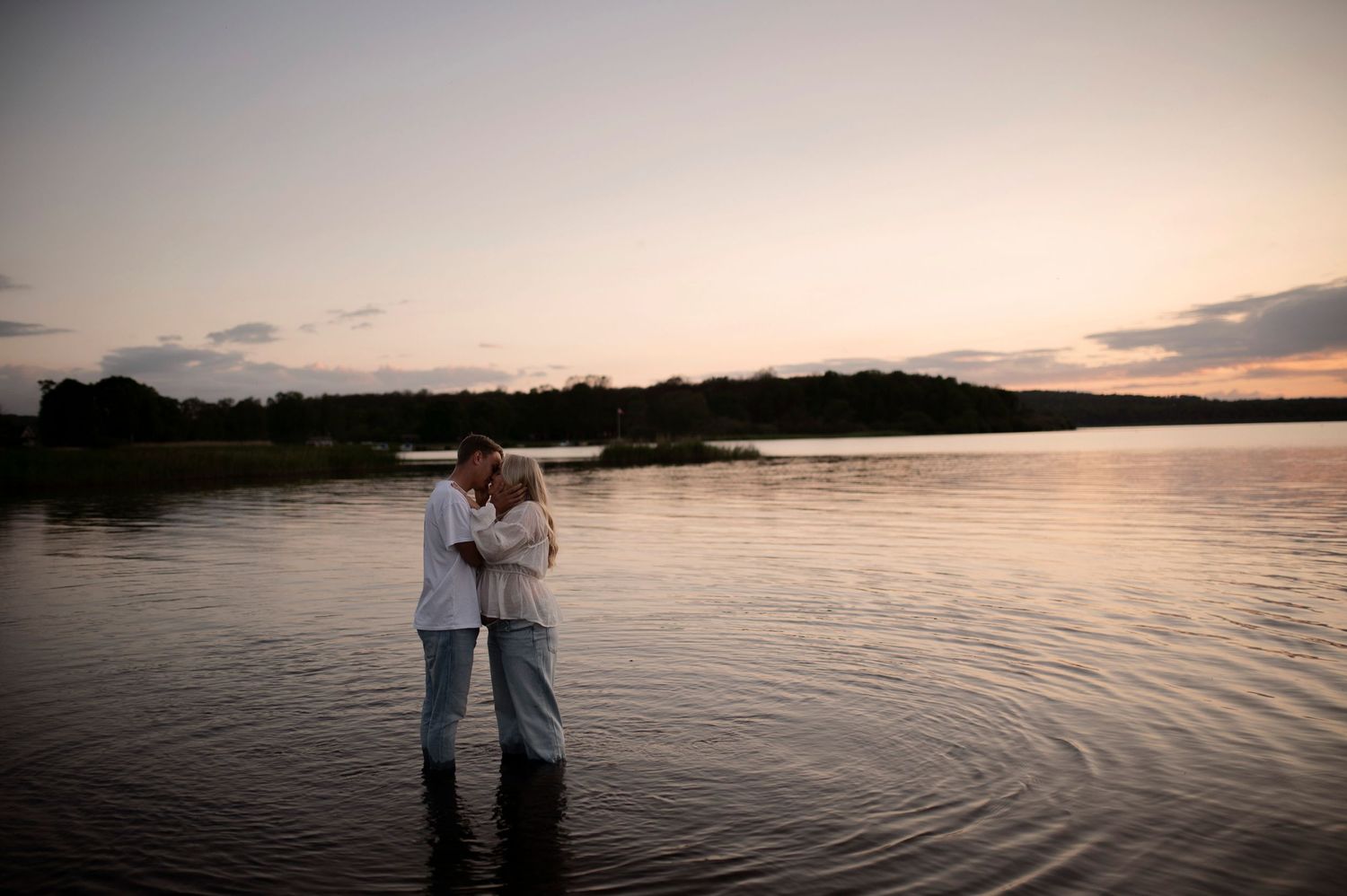 Silhouettes of two people embracing against a peaceful lakeside sunset.
