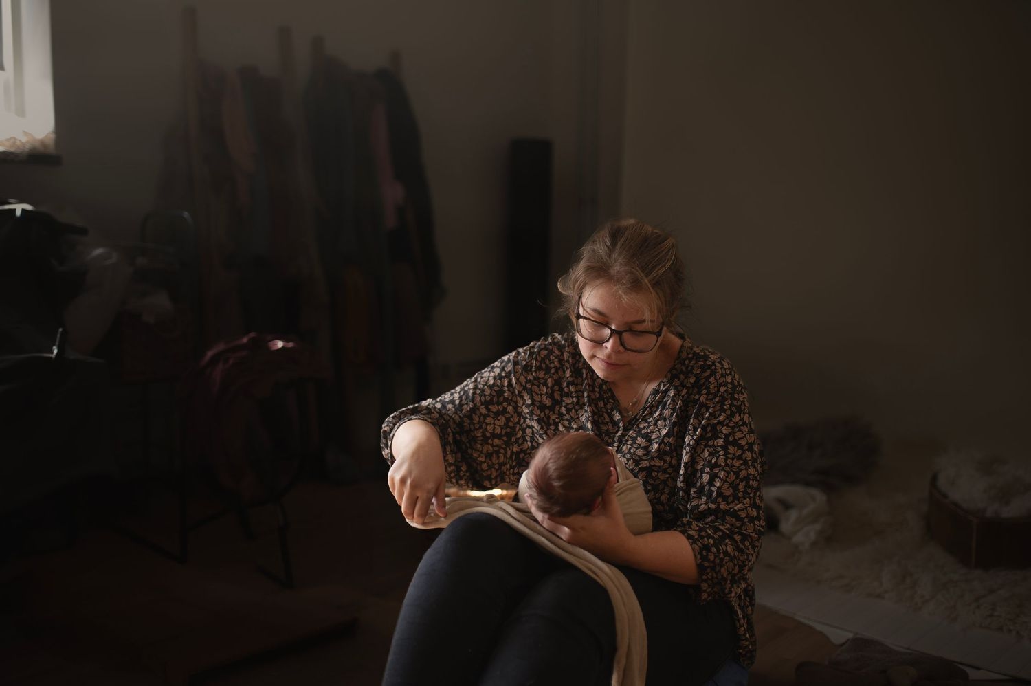 Woman in glasses holding a newborn baby while seated in a dimly lit room.