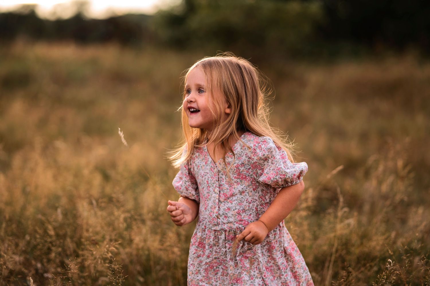 Child in a floral dress twirling and laughing in a summer meadow at sunset.