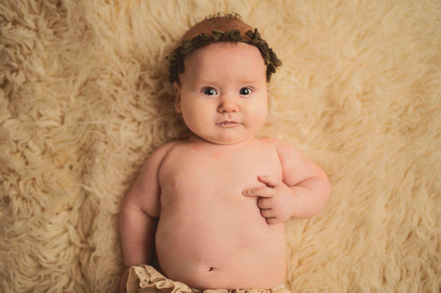 Infant with curly hair lying on soft beige carpet.