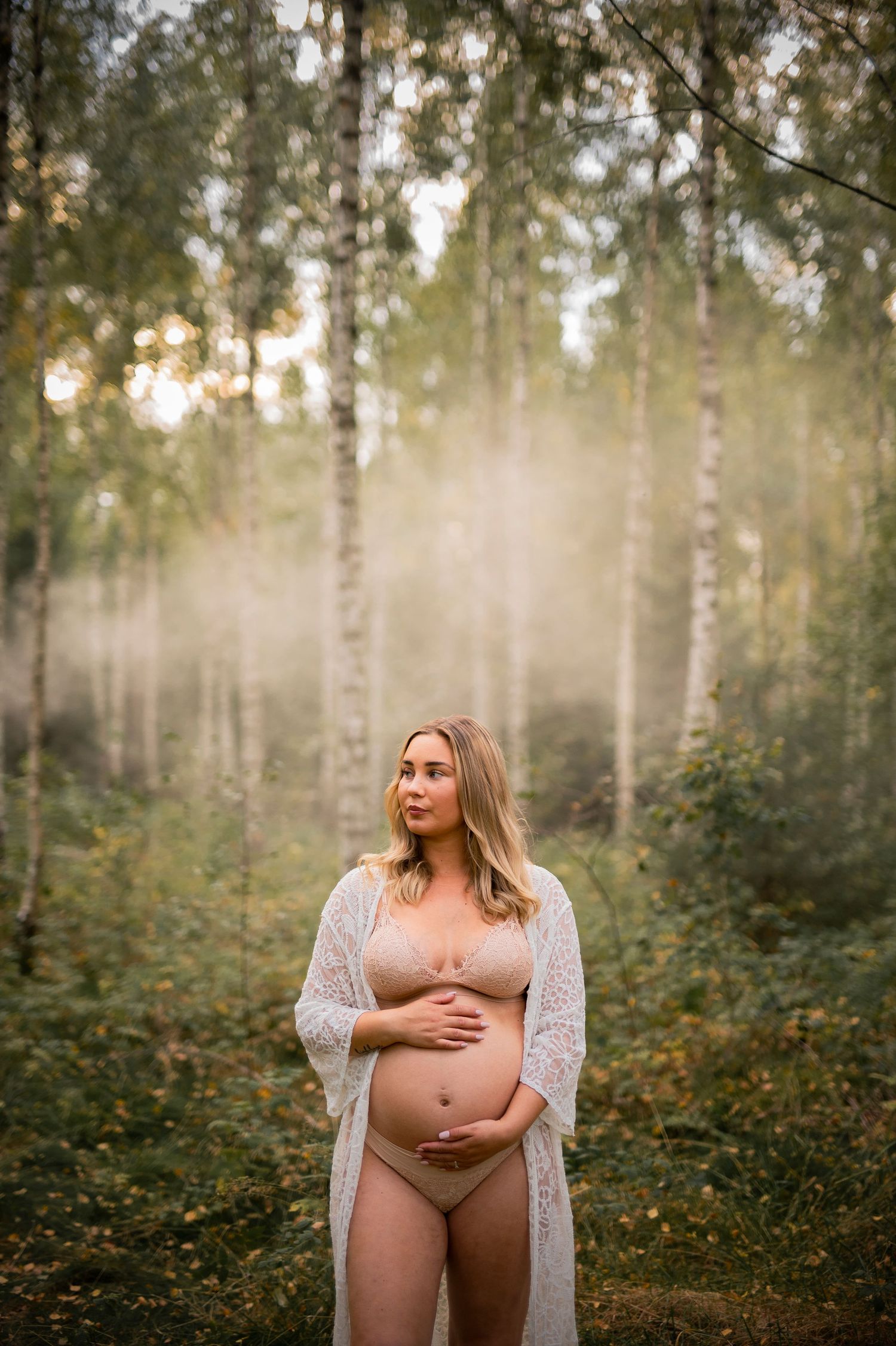 Maternity portrait in misty birch forest with soft natural lighting.