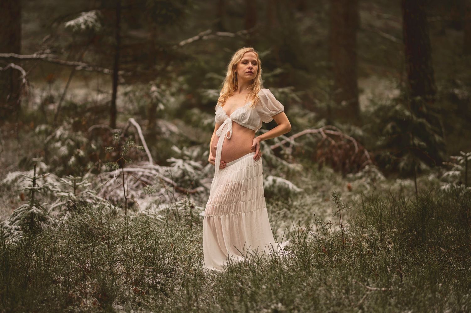 Vacker gravid kvinna på fotografering i en skog med mossa. Fotograf är Lovestories By Sara.