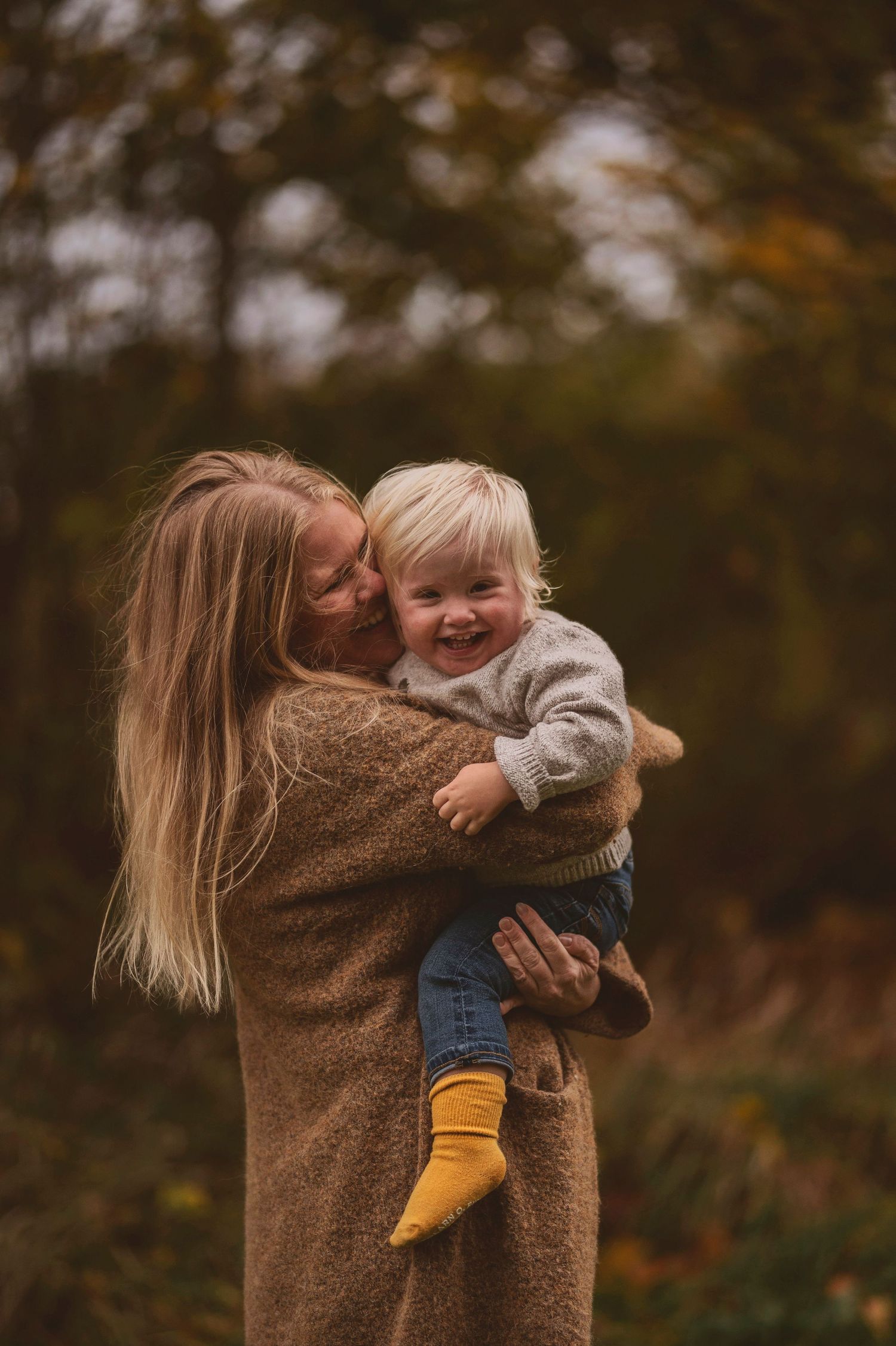 Tender moment captured between adult and child wearing yellow socks in fall forest setting.