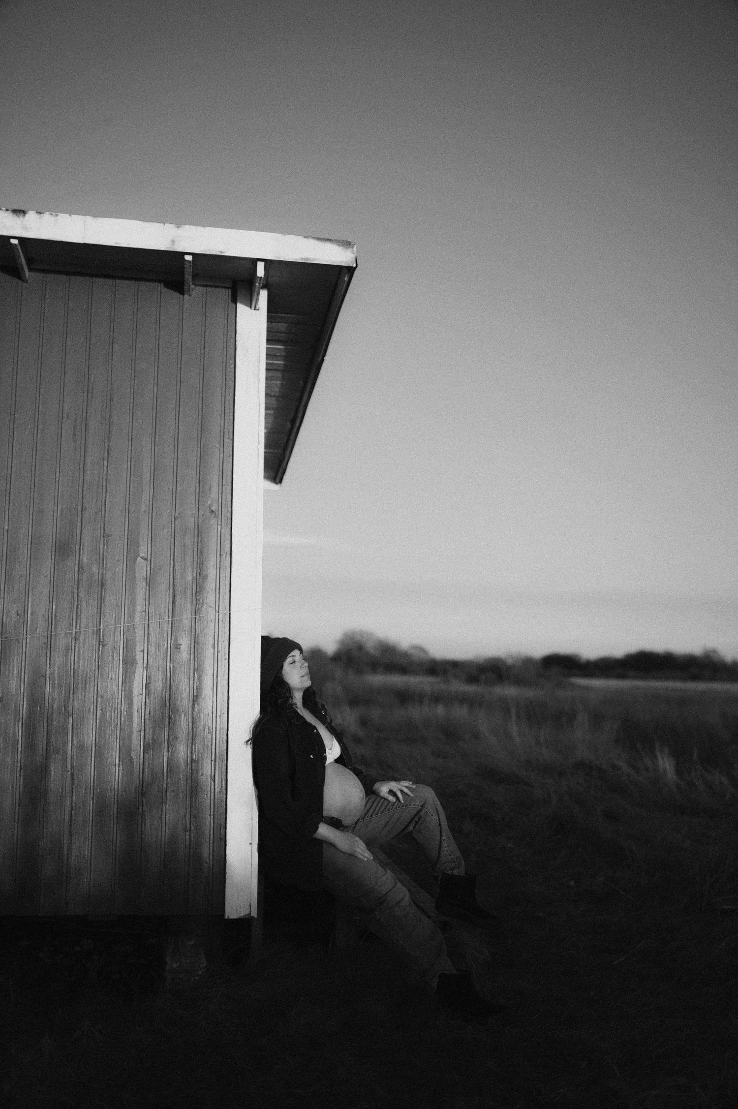 Artistic black and white maternity photo against rustic wooden building.