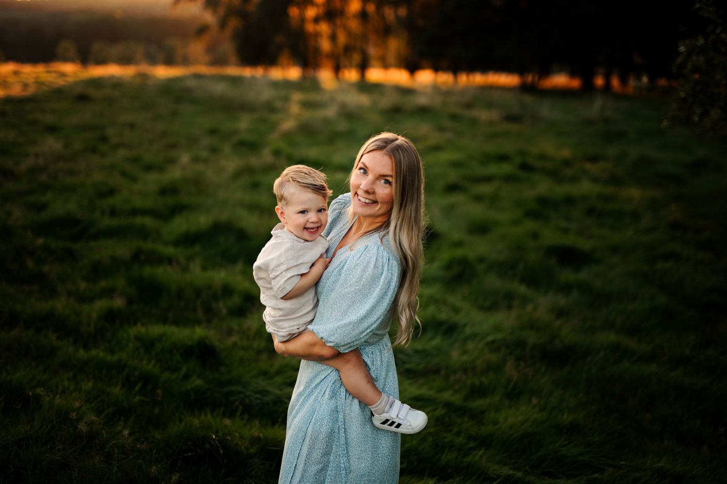 Joyful outdoor portrait against a backdrop of golden sunset light and green grass.