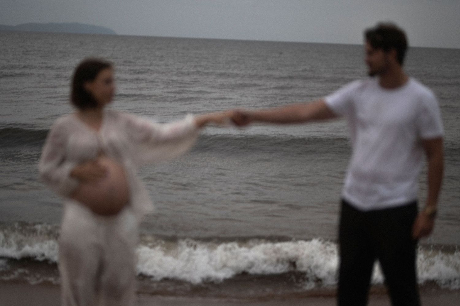Artistic blurred photo of a couple holding hands on a beach with waves in the background.