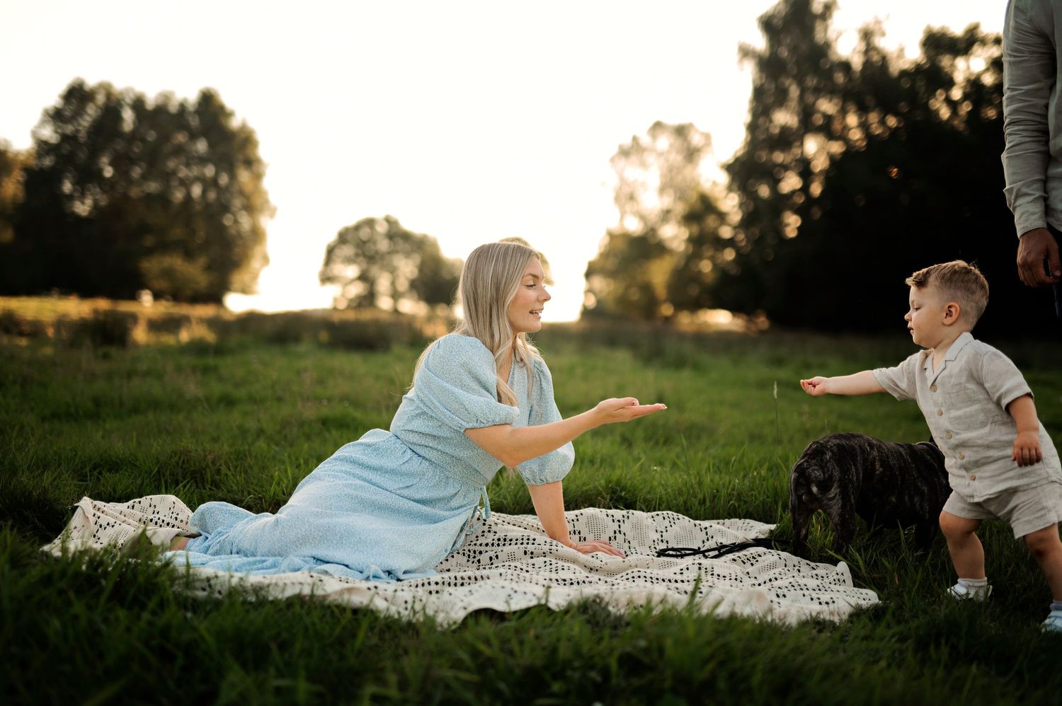 Relaxed family moment on picnic blanket in grassy field at sunset.