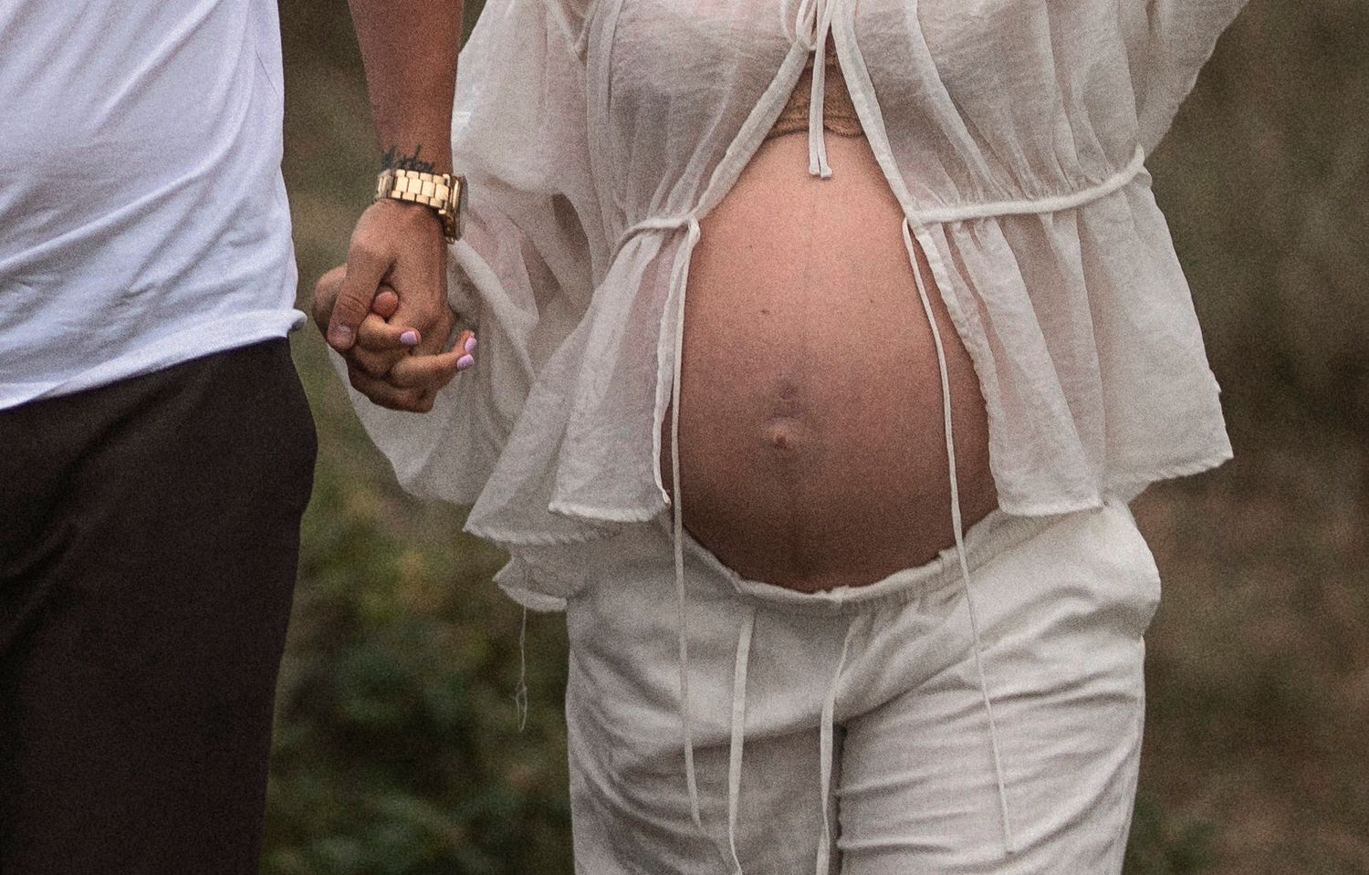 Close-up of joined hands and a baby bump in delicate white fabric.