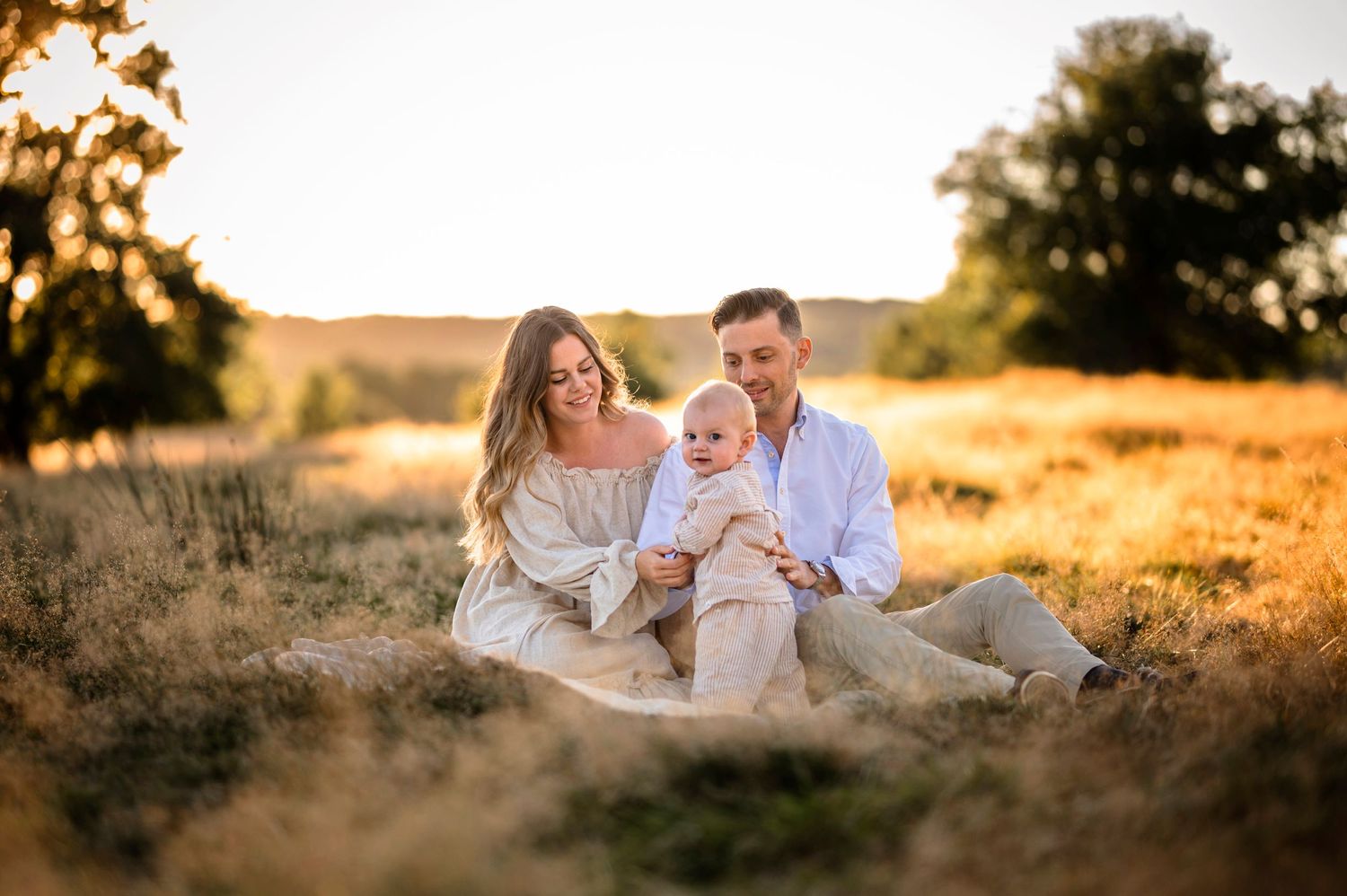 Family sitting together on blanket in golden field at sunset.