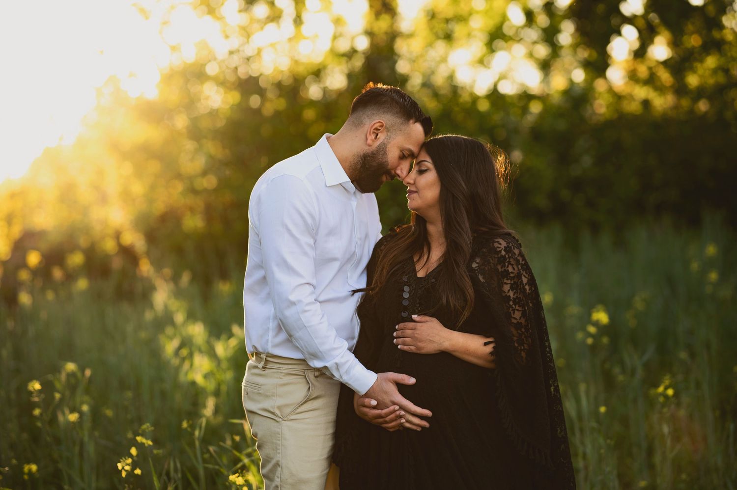 Romantic maternity photo of couple in flowering meadow at golden hour.