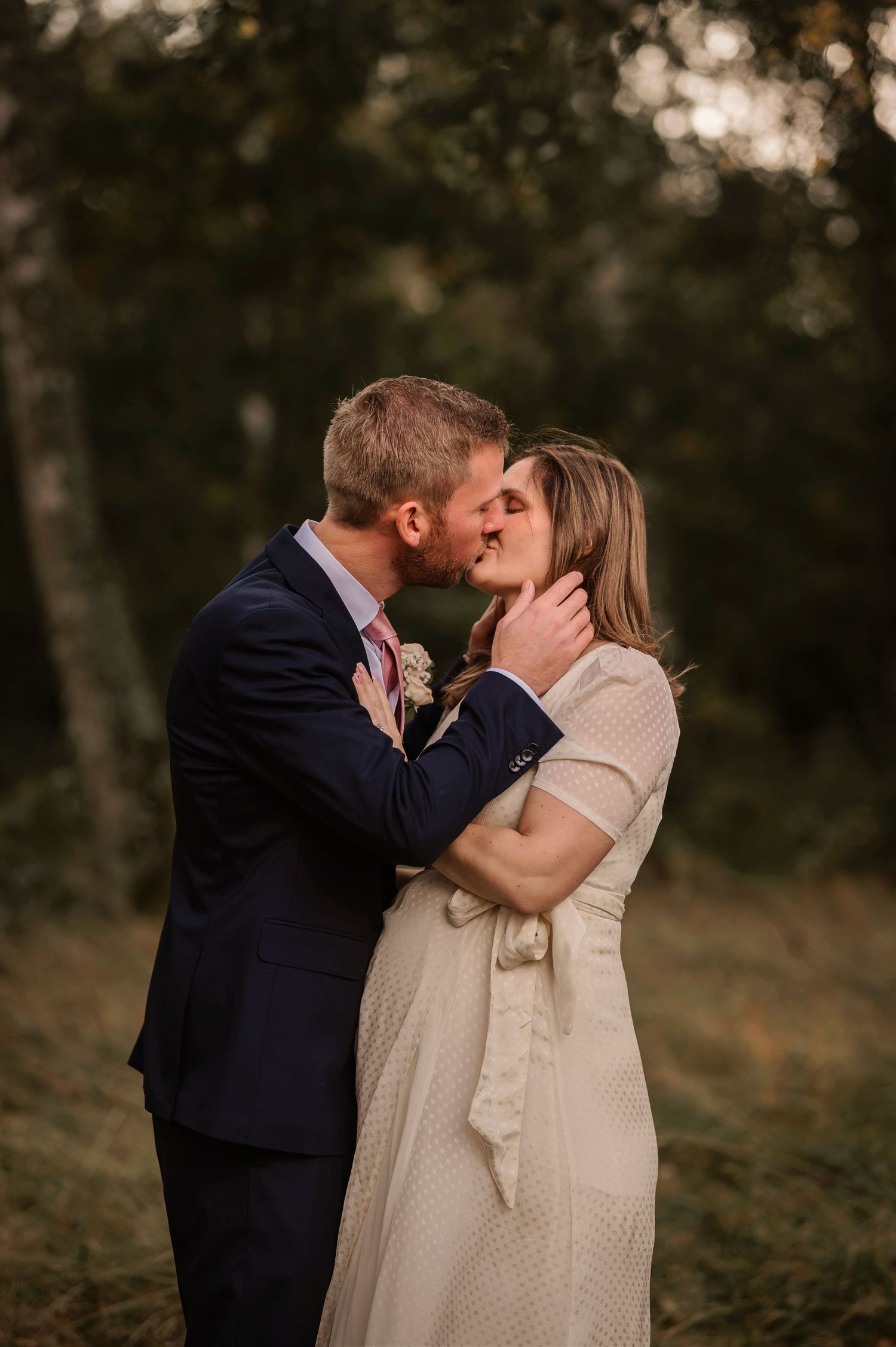 Romantic outdoor wedding portrait of couple kissing in autumn setting.