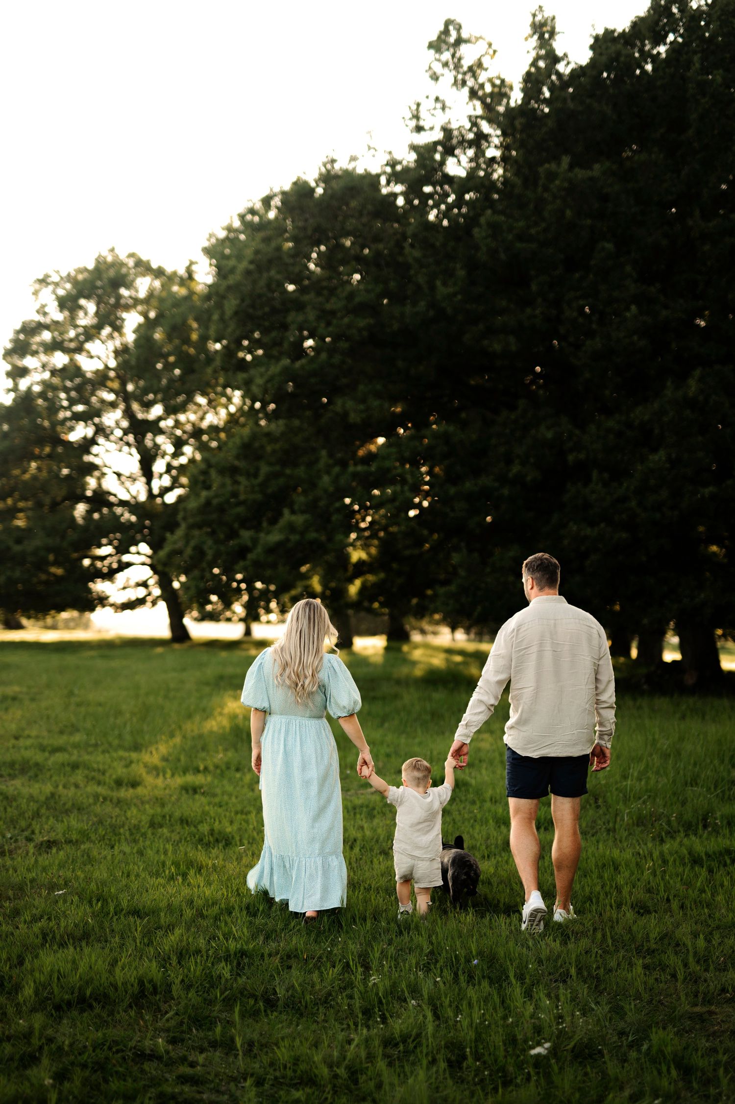 Family walking together through a grassy meadow at sunset with trees in the background.