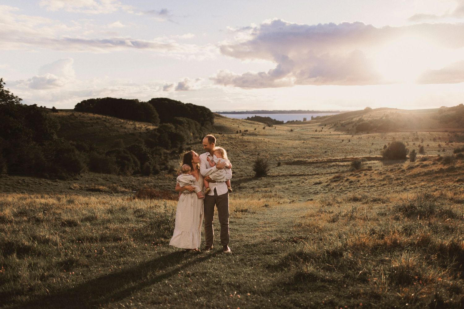 Family standing together in golden sunset light on grassy hillside.