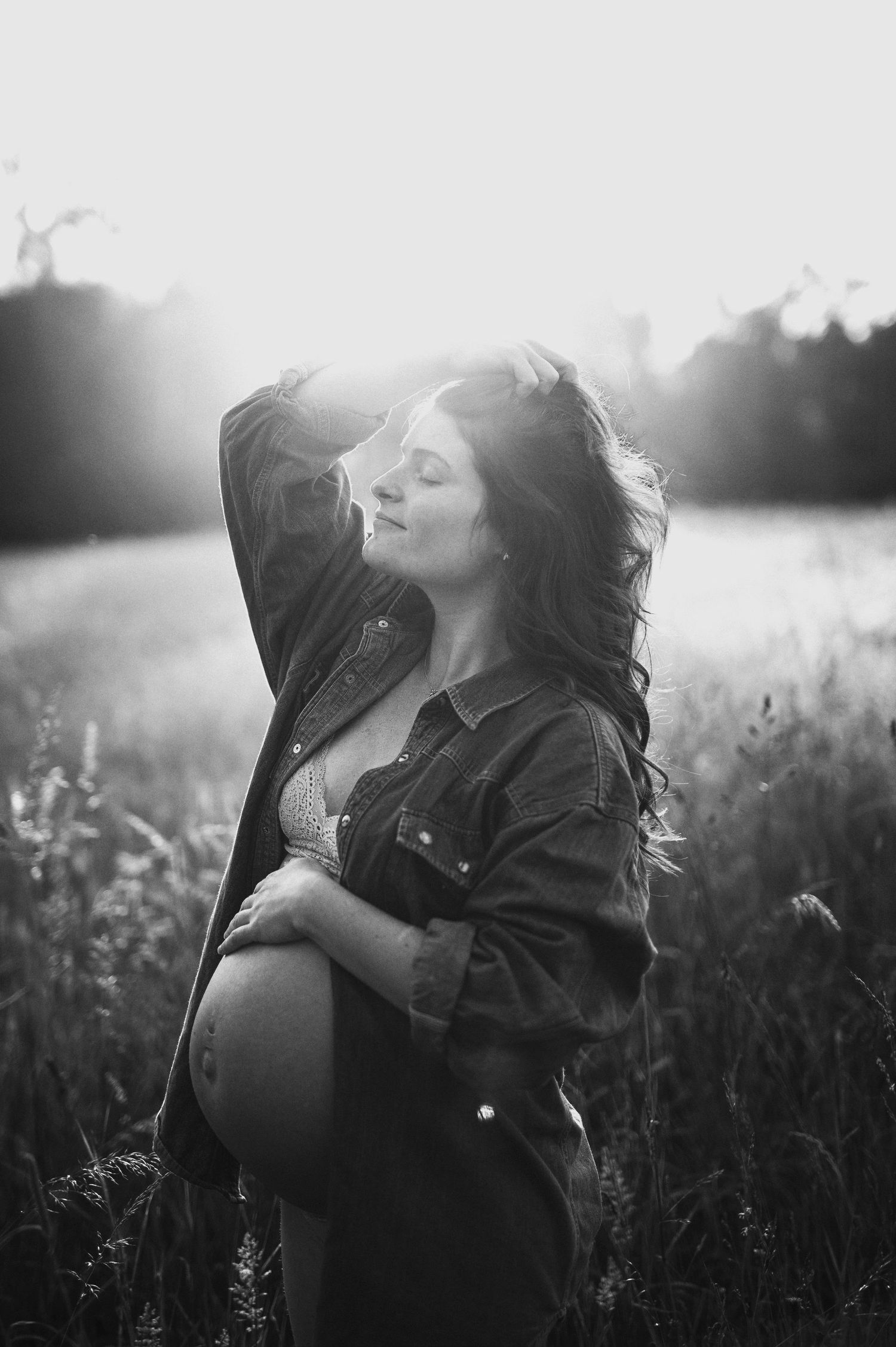 A black and white maternity portrait captures a peaceful moment in a natural setting.