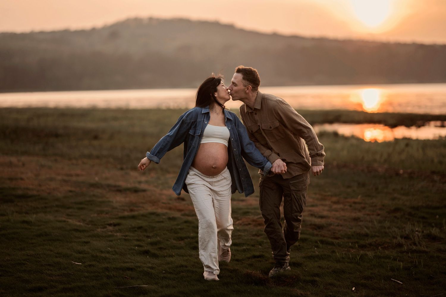 Two people walk hand in hand along a scenic shoreline at sunset creating a romantic silhouette against the golden sky.