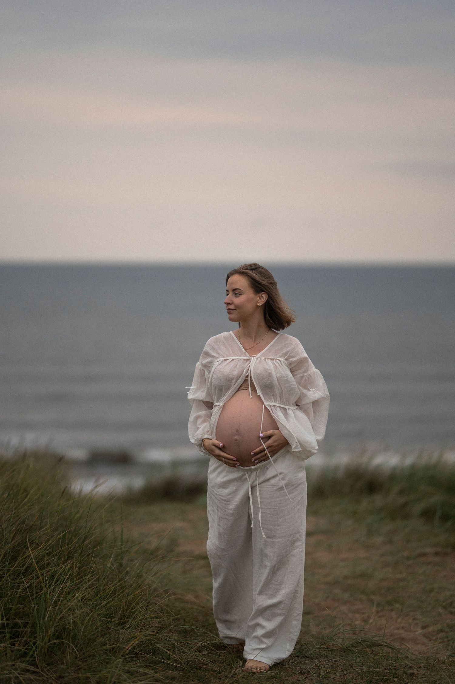 A maternity photoshoot captures a peaceful moment overlooking the ocean at dusk.