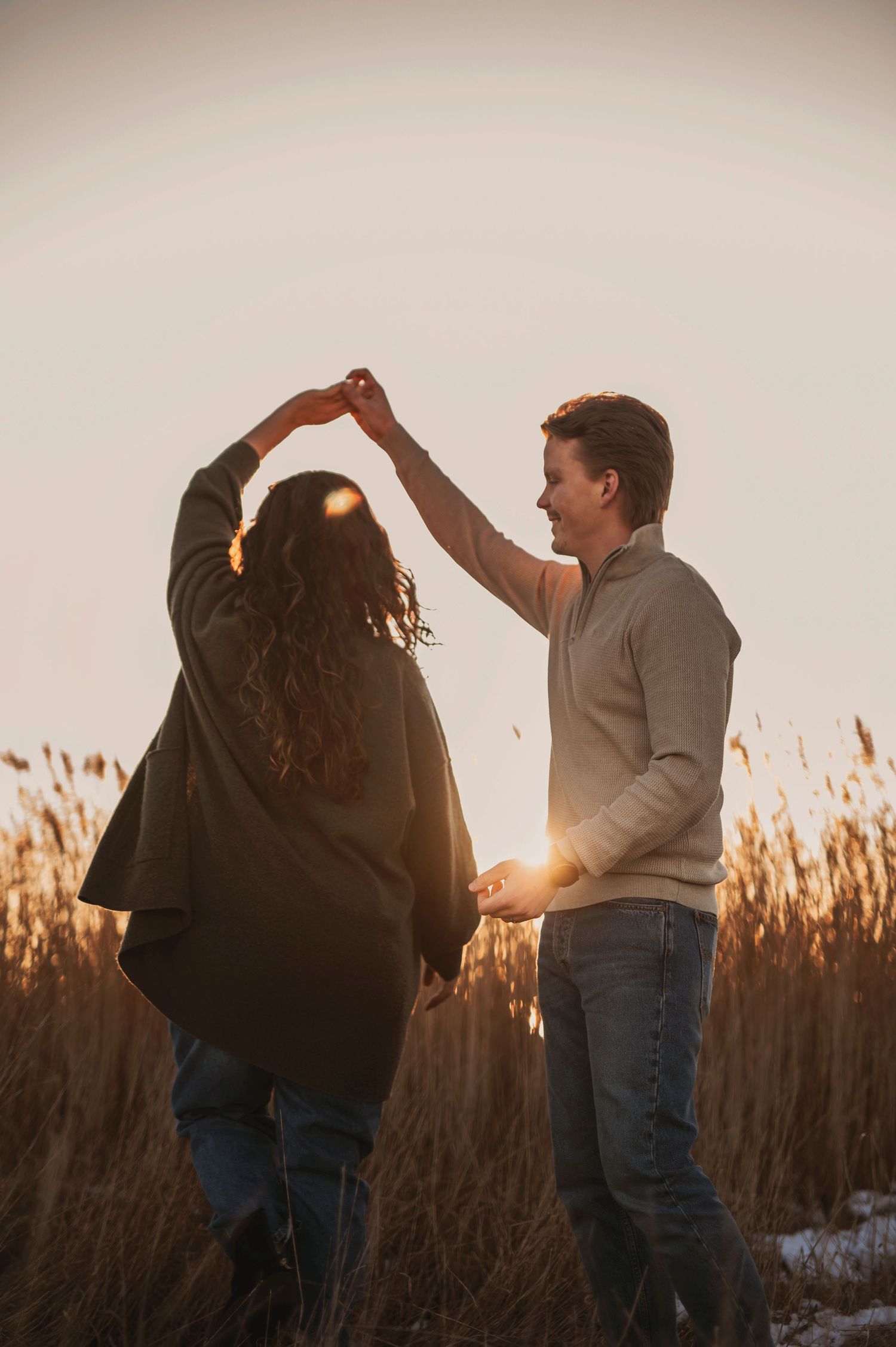 Sunset maternity photo of couple dancing among tall grass in winter.