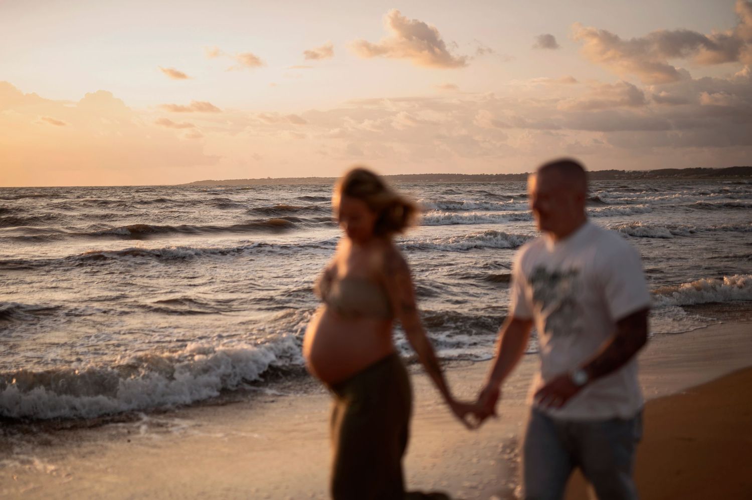 Couple walking hand in hand along a sandy beach at sunset with waves crashing on the shore.